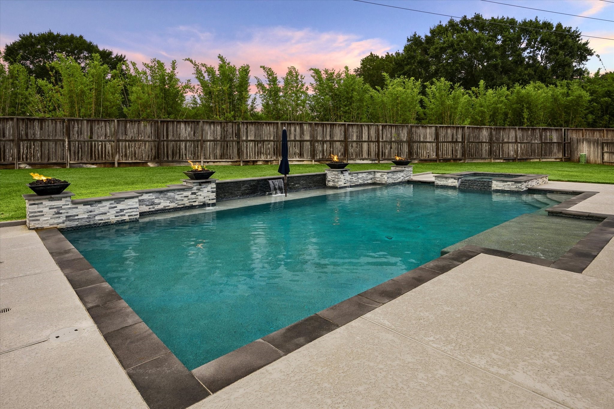 This expansive sparkling pool, framed by elegant stone accents, cascading water features, and dramatic fire bowls that create a stunning ambiance from day into evening. The generous pool deck provides plenty of room for lounging and entertaining, while the lush, fully fenced yard and mature greenery create a peaceful sense of privacy.