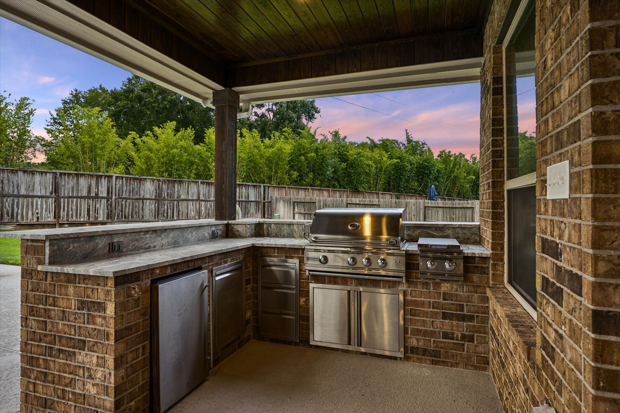 This impressive, covered kitchen features a built-in stainless-steel grill, side burner, refrigerator, and generous prep and serving space. This covered design provides shade and comfort for year-round gatherings with ample counter space that makes poolside dining and entertaining a breeze.