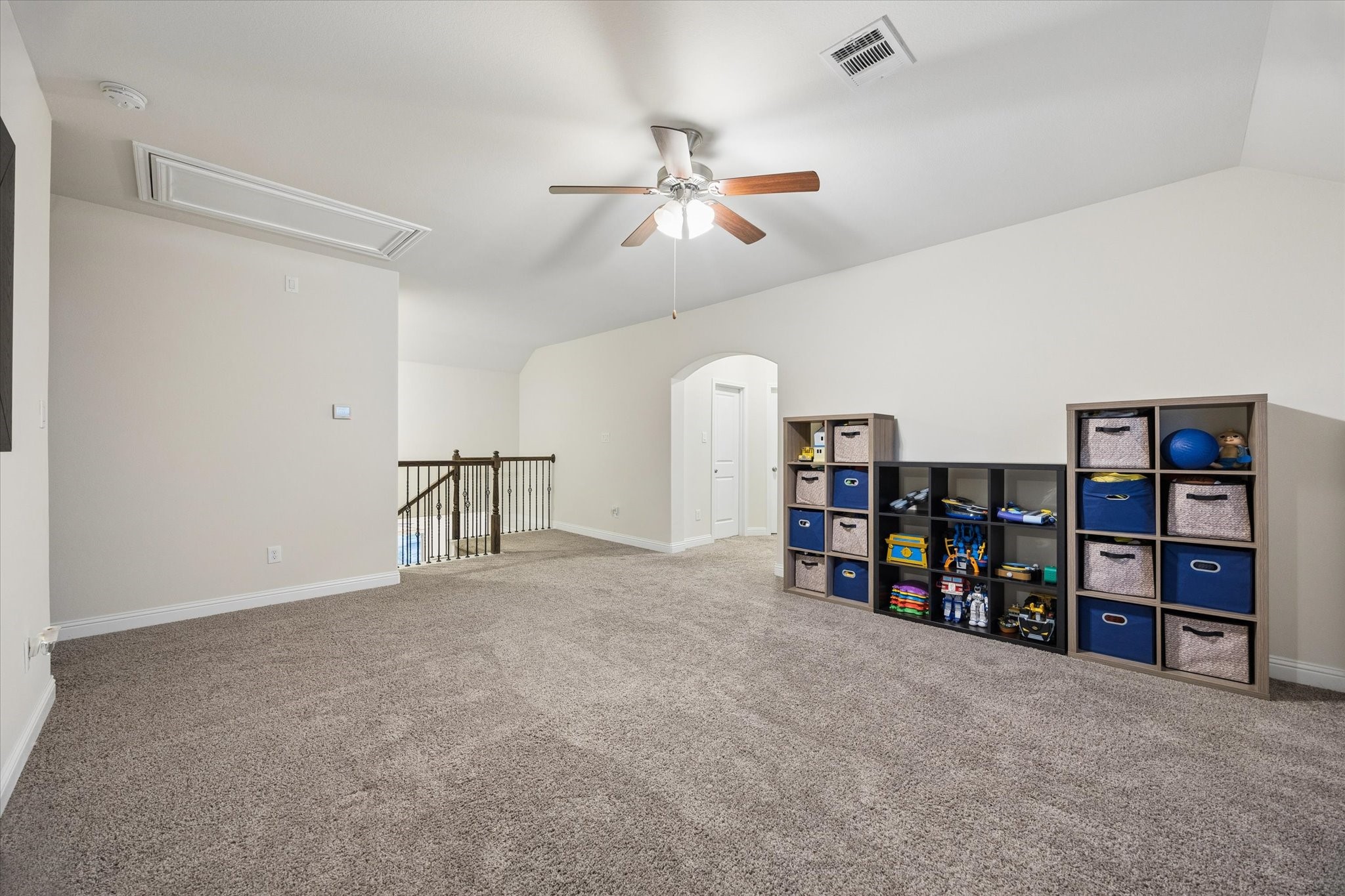 Spacious and versatile game room offering an open layout, plush carpeting, and plenty of room for recreation, lounging, or space for kids to play endlessly. The open staircase and arched doorway add architectural character. A ceiling fan and neutral finishes complete this inviting upstairs retreat.