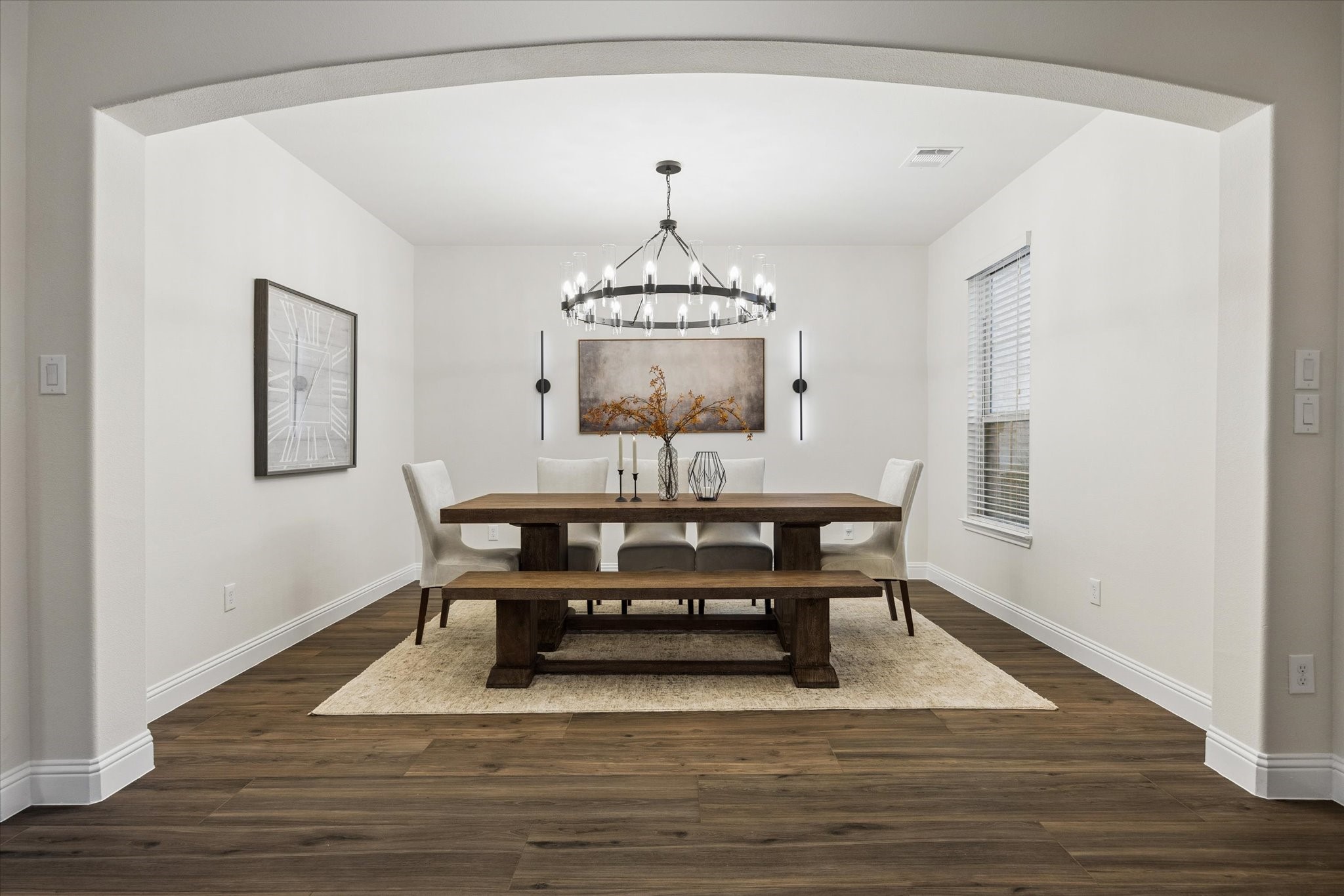 Welcoming dining area featuring a classic arched entry, warm wood flooring, and large enough to fit a substantial size wood dining table with bench seating. Neutral recessed details. This is an ideal space for everyday meals or entertaining.