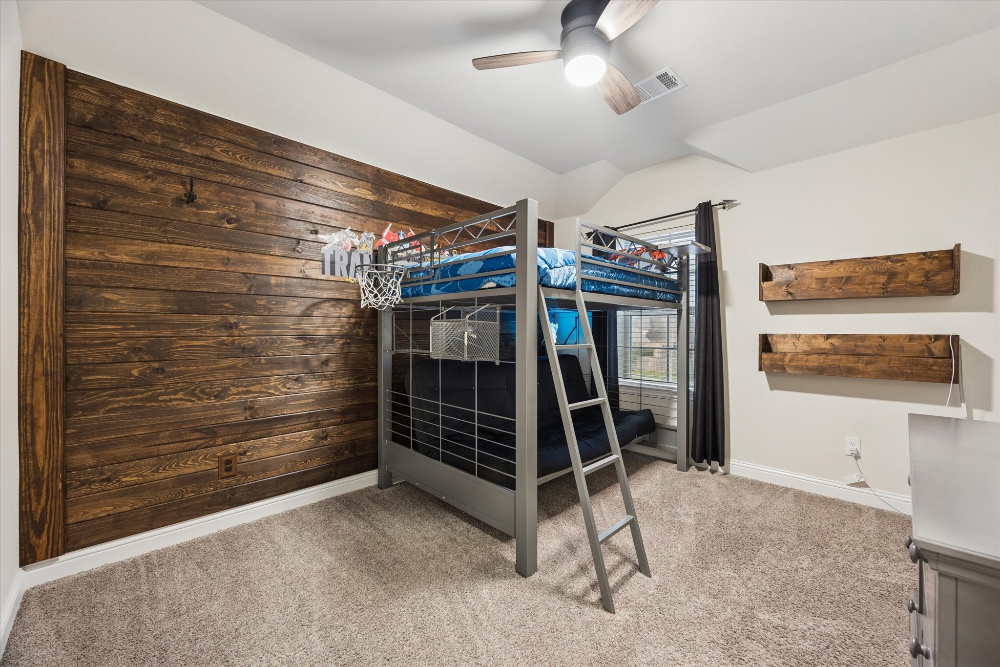 This inviting bedroom offers a warm and playful retreat, featuring a striking custom wood accent wall that adds rustic character and visual appeal.