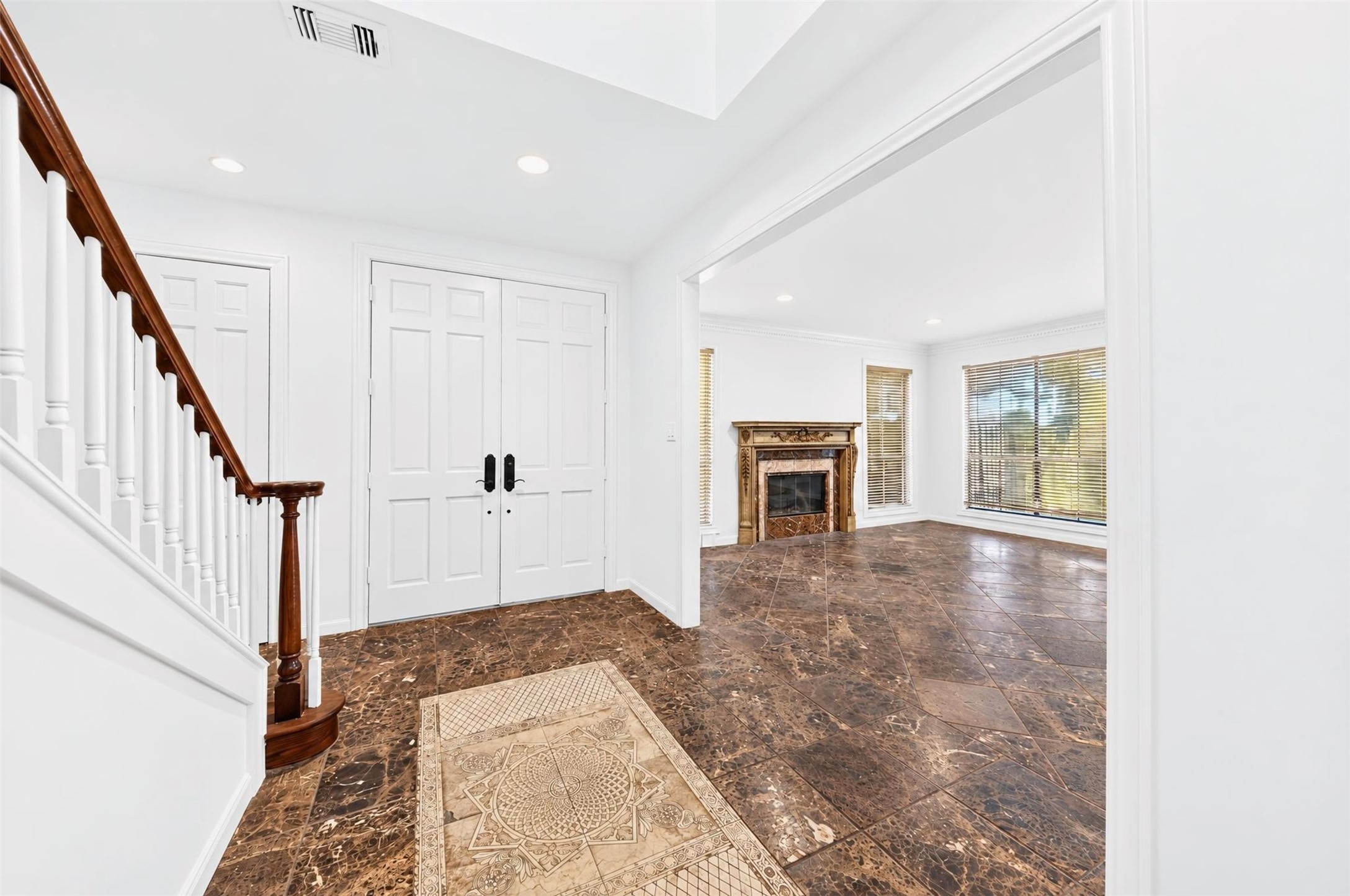Foyer view shows double entry doors, a decorative floor inset and the adjacent living room.