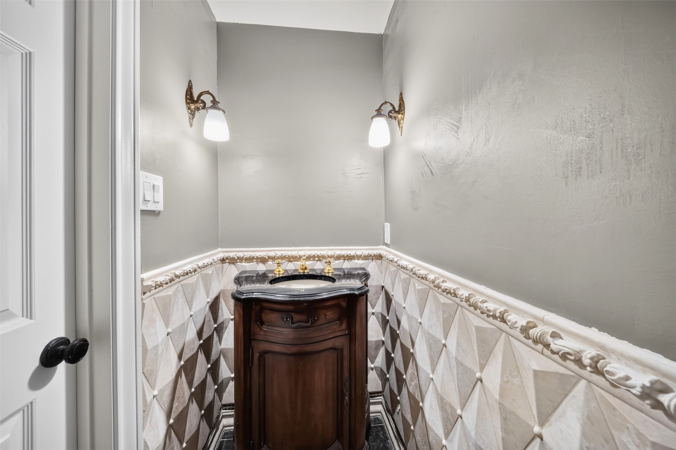 Powder room with a furniture-style vanity, wall sconces and patterned wall tile.