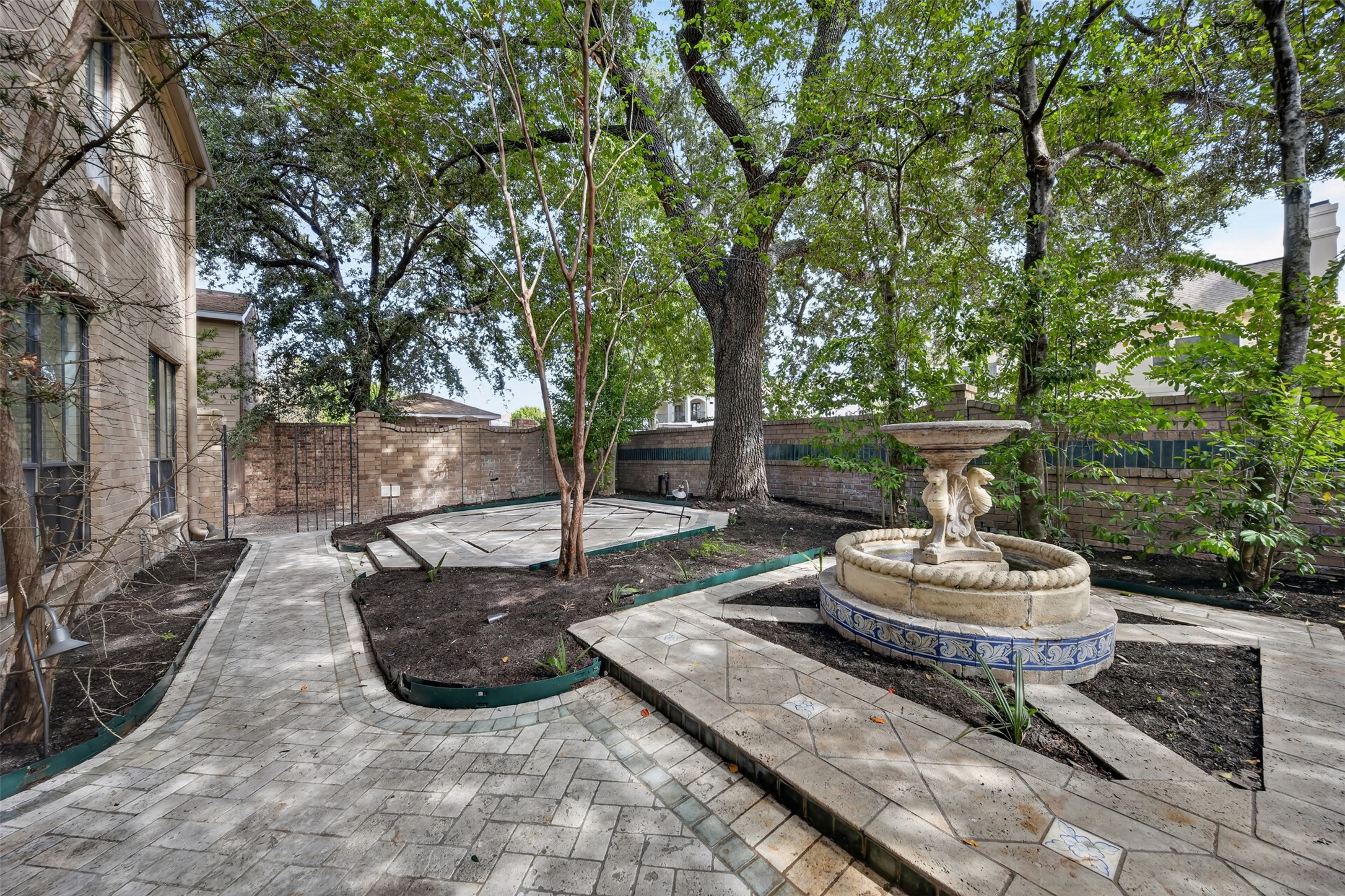 Paved courtyard paths wind around tree beds, with a fountain and brick boundary wall.