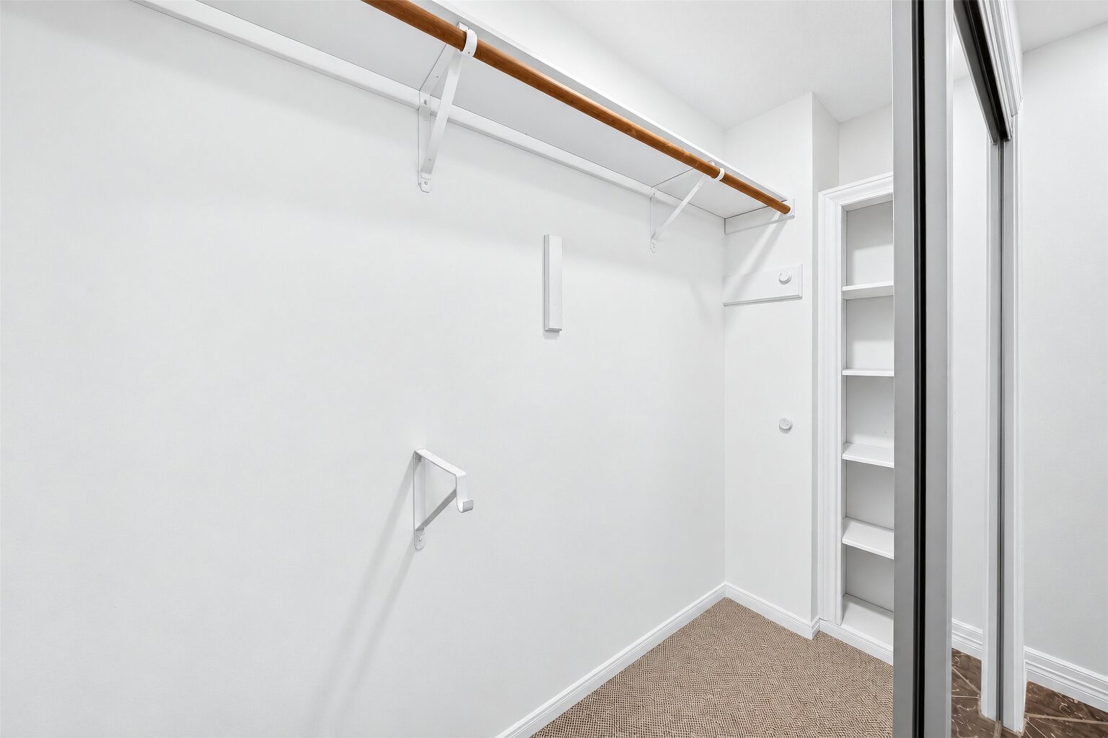 Carpeted walk-in closet with a long hanging rail, upper shelf and side shelving.