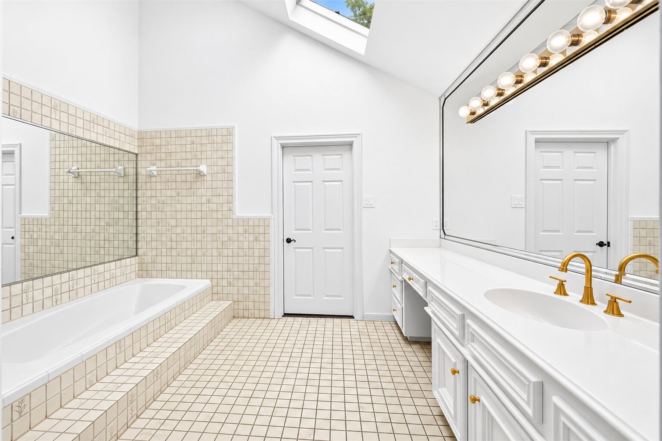 Bathroom with a tiled tub surround, long vanity and a high window above.