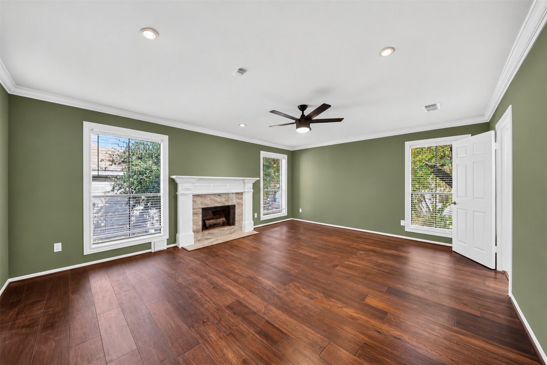 Primary bedroom windows flank the fireplace, with wood-tone flooring and recessed lighting.