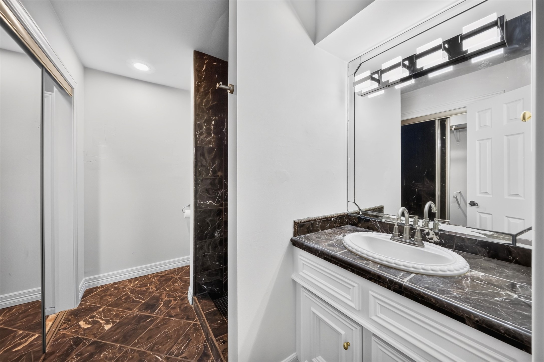 Bathroom vanity with an oval basin, dark counter and mirrored closet doors nearby.