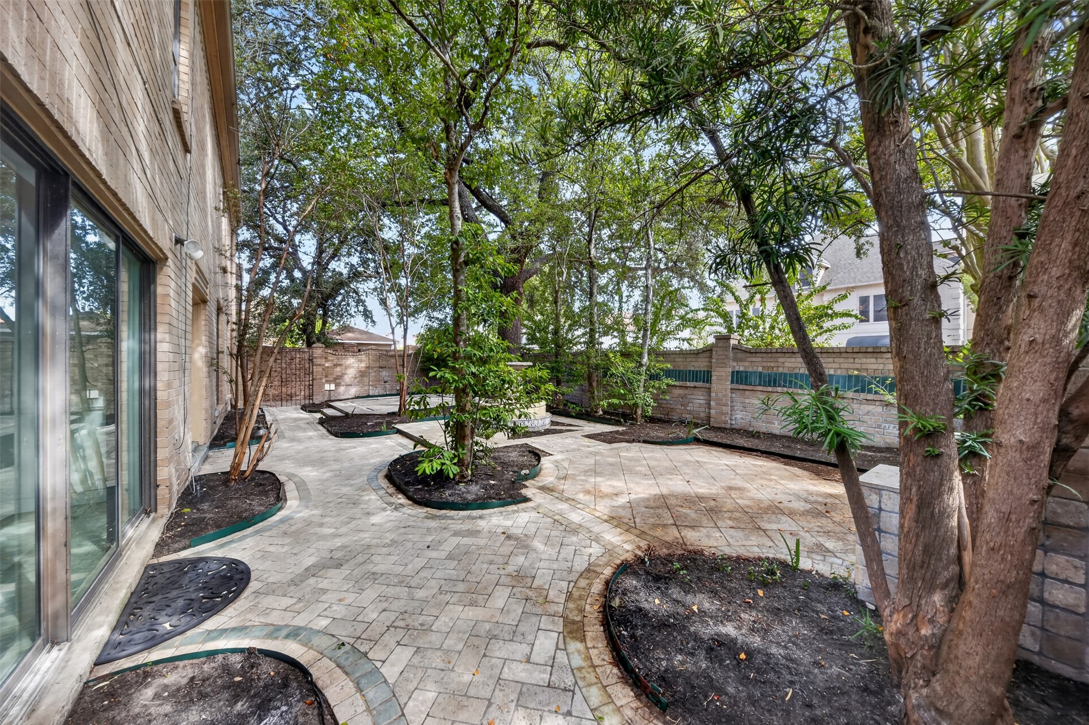 Curving paved walkway follows the home's windows beneath a canopy of mature trees.