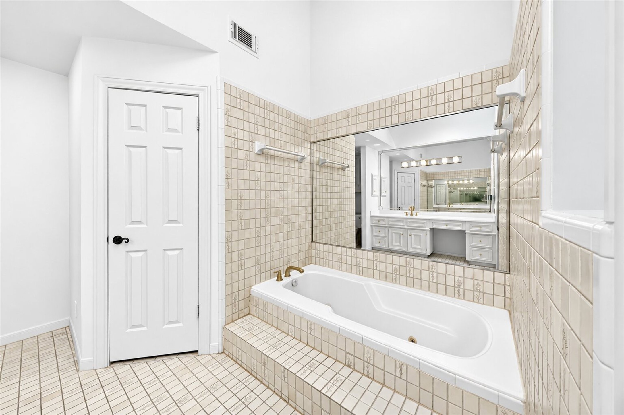 Inset bathtub with a tiled surround, wall mirror and nearby storage door.