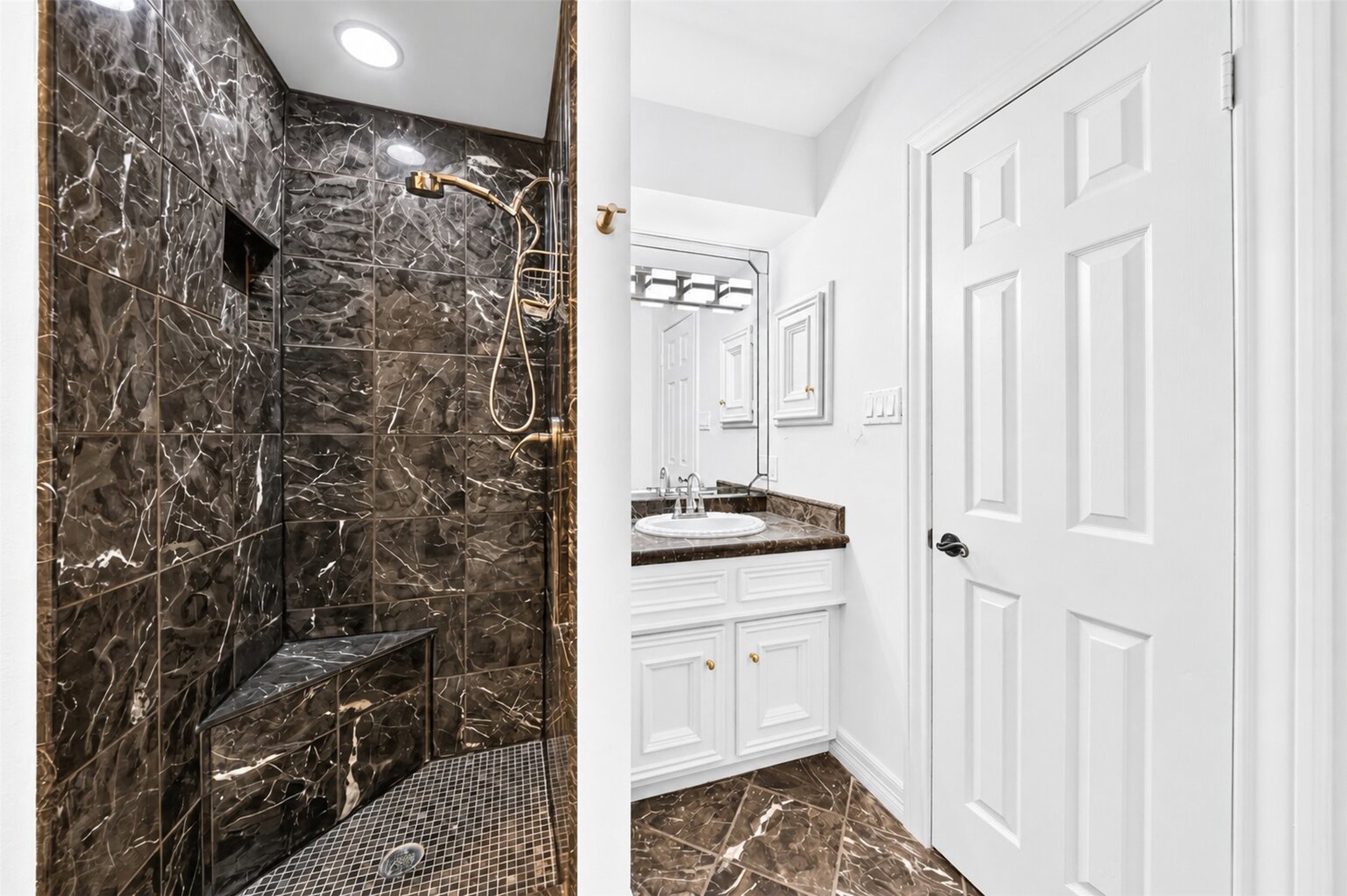 Dark-tiled shower with a built-in bench, recessed niche and handheld fixture.