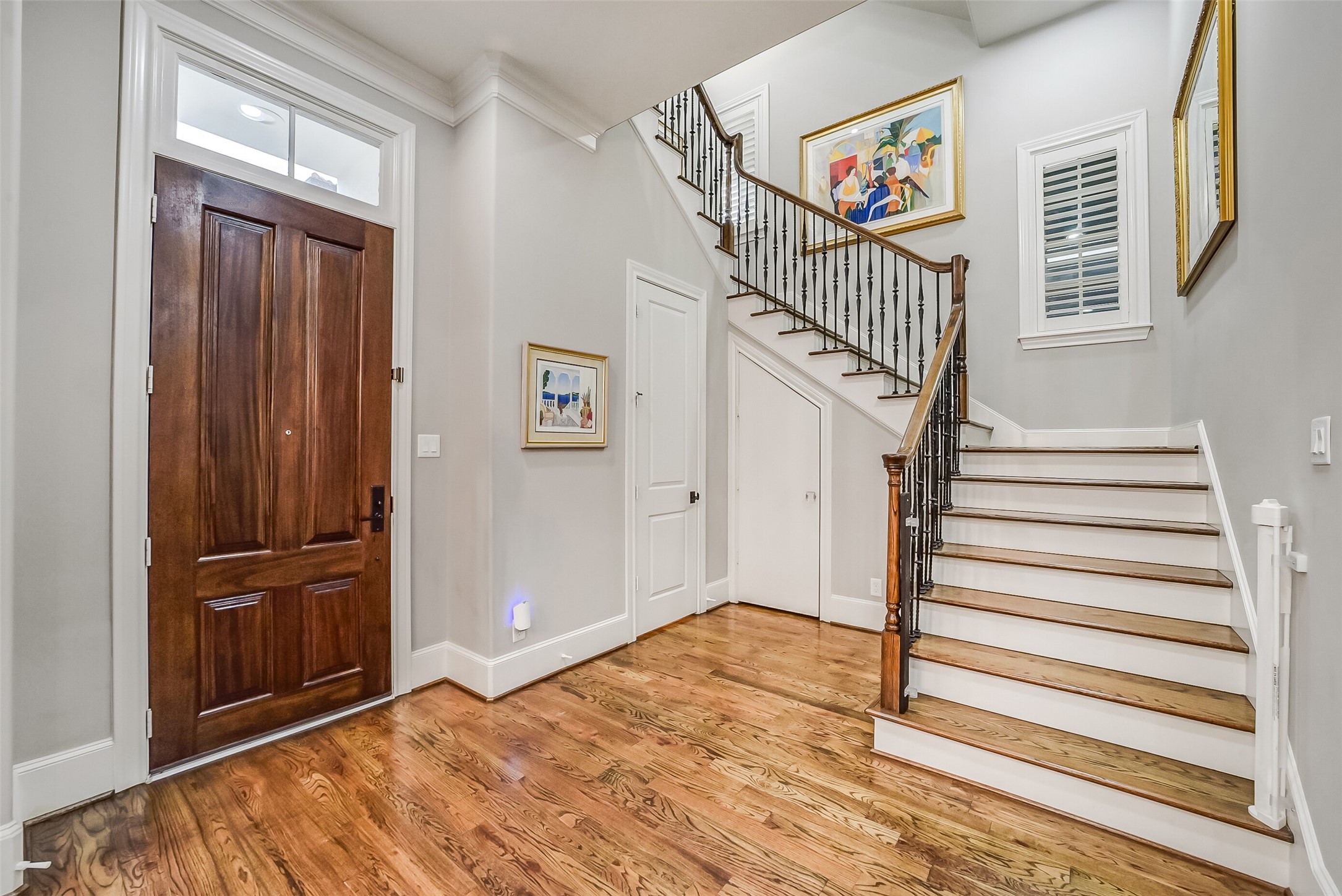 Make a grand entrance through a rich, stained wood front door topped with a transom window. The foyer opens to hardwood floors and a sweeping staircase with a wrought-iron and wood railing, wood-shuttered windows, and crown molding. Smart under-stair storage adds everyday convenience.
