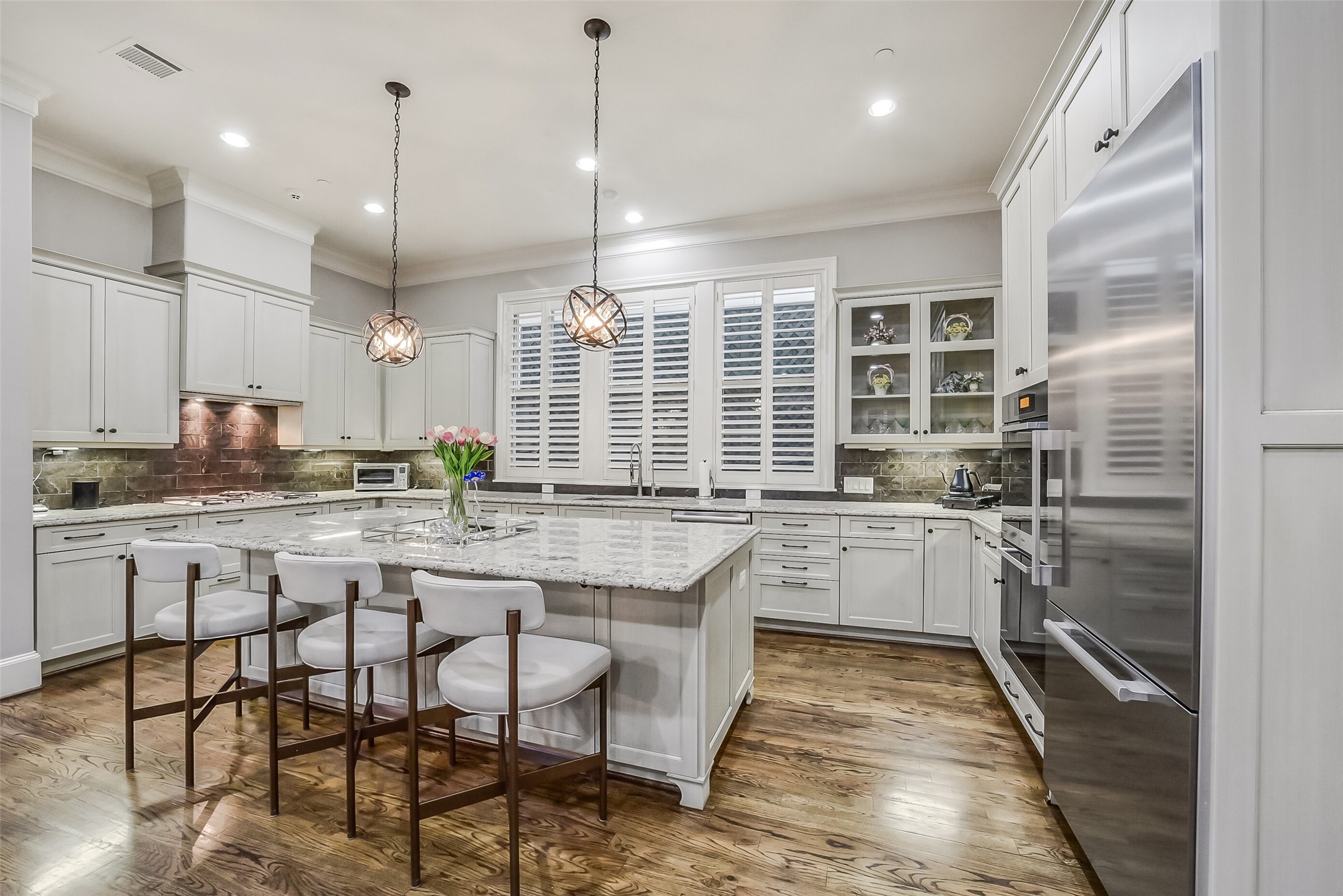 Exceptional chef's kitchen featuring gleaming cabinetry, spacious countertops, and a large center island with a breakfast bar and elegant pendant lighting. Bright natural windows complete this sophisticated and functional design.