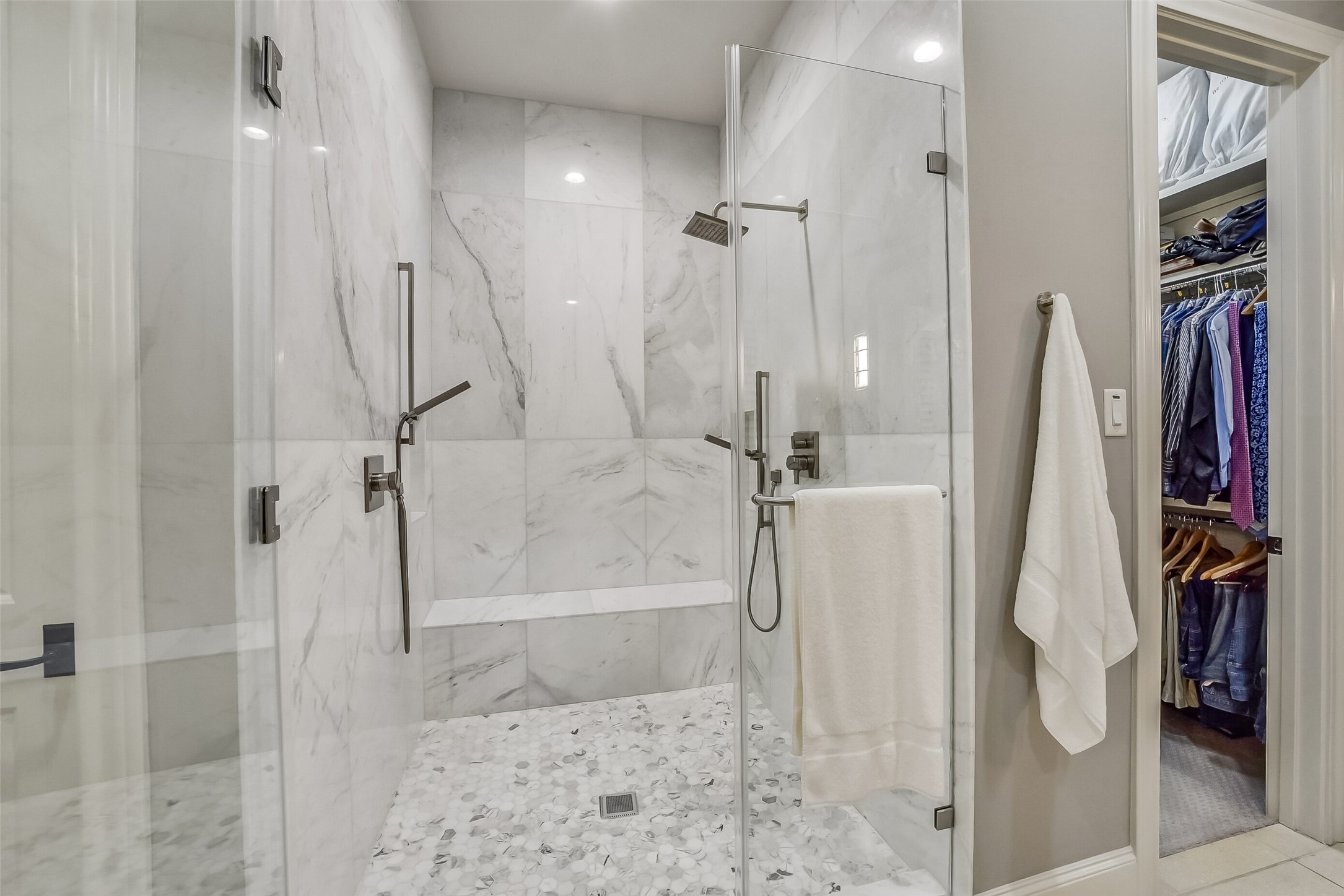 Beautiful walk-in shower showcases frameless glass enclosure and a built-in bench for added comfort and convenience. Dual shower fixtures, including a rainfall showerhead and handheld sprayers, complement the sophisticated design.