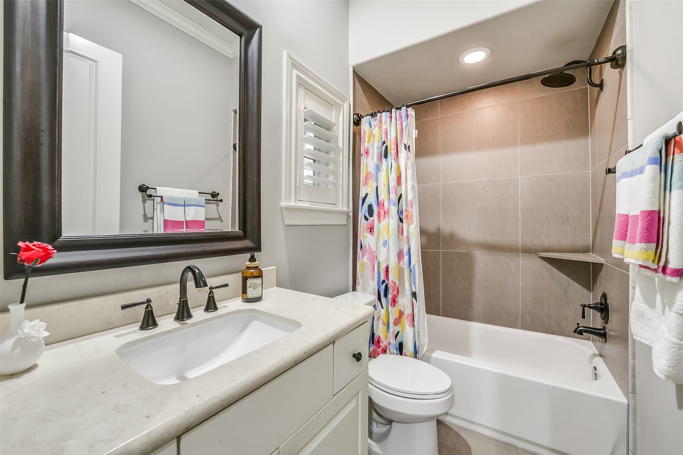 Ensuite bath features a vanity, a charming window with plantation shutters, and a tub/shower combo complete with a built-in shelf for added convenience.