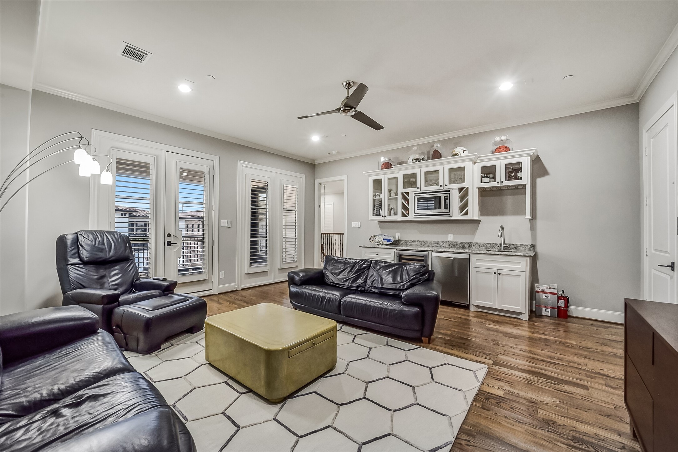 This spacious third-floor game room offers the perfect setting for entertaining. A well-appointed wet bar features custom cabinetry, a beverage refrigerator, dishwasher and a built-in microwave for effortless entertaining. French doors with plantation shutters open to a private balcony.