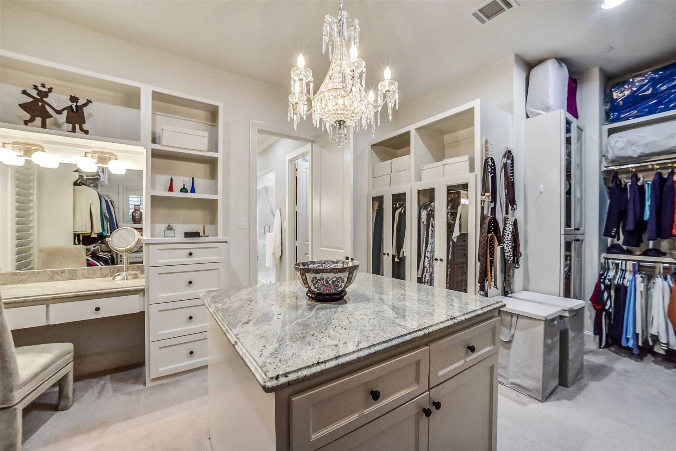 One of two expansive walk-in closets offers an exceptional blend of luxury and functionality. A generous center island, custom built-ins, and hanging space provide additional storage and a convenient space for wardrobe planning and organization. A dedicated vanity with mirror creates the perfect space for getting ready in style.