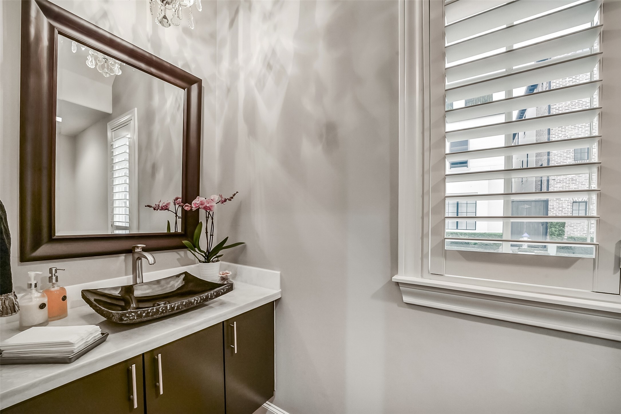 An elegant half bath featuring a rich espresso-finished vanity, a sophisticated dark vessel sink, and crisp plantation shutters, creating a stylish and inviting space for guests.