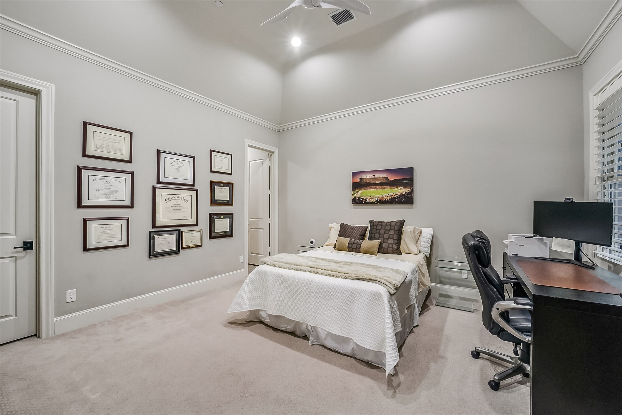 Very spacious secondary bedroom with soaring vaulted ceilings. A ceiling fan and large window with shutters provide comfort and natural light, with room for a home office setup.