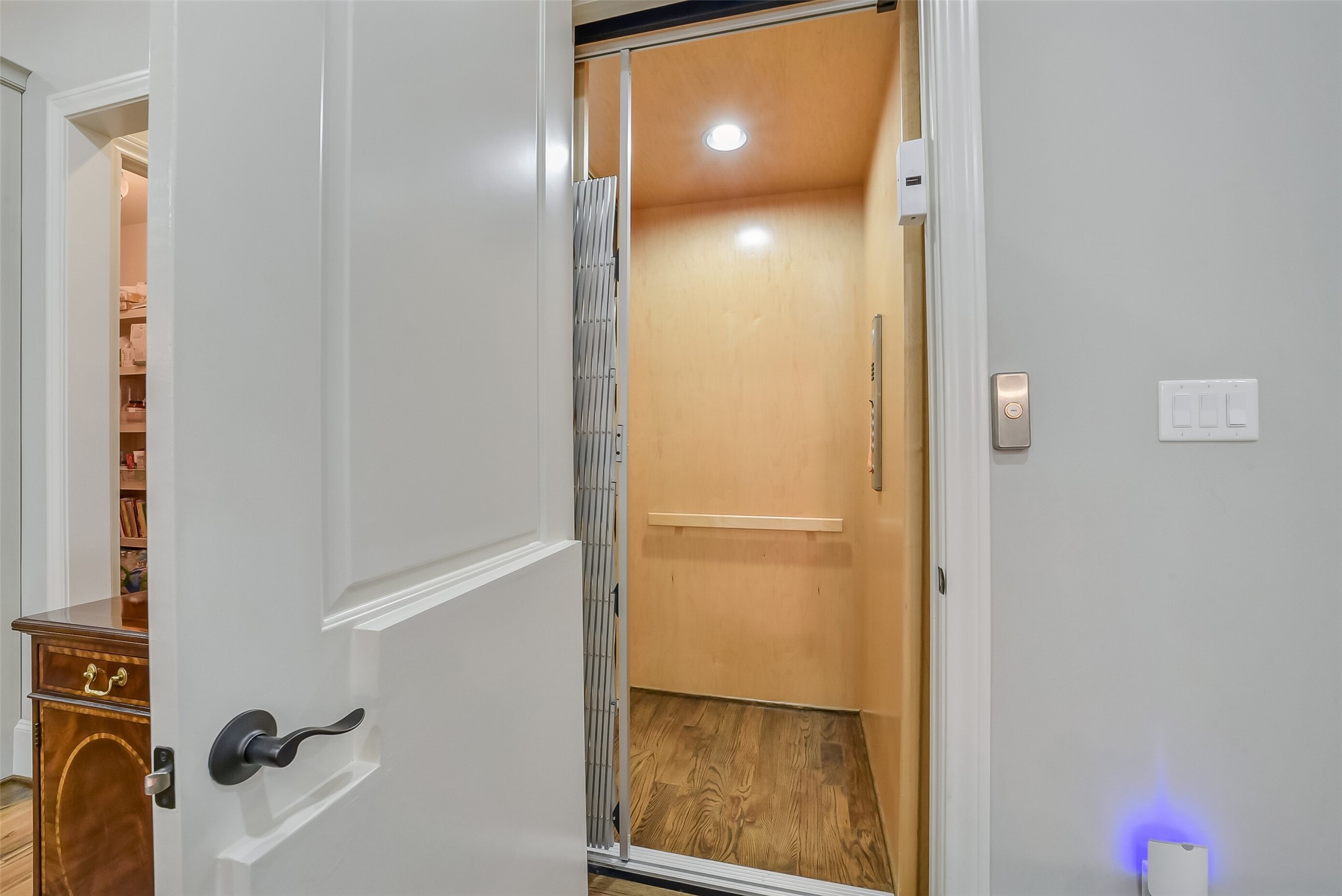 Convenient in-home elevator with warm wood paneling, a hardwood floor, and a collapsible gate, making it easy to move between levels with luggage, or laundry. It also adds long-term accessibility and everyday ease.