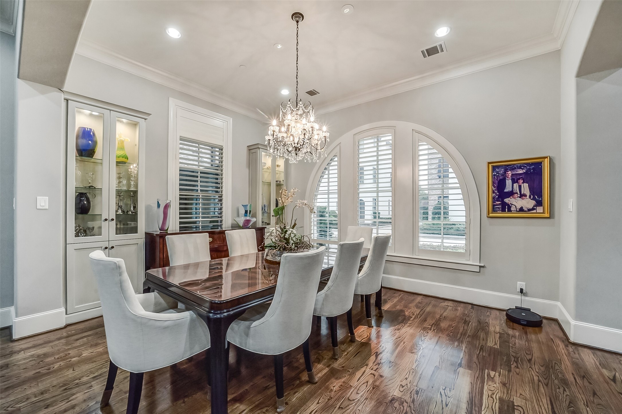 Elegantly appointed formal dining room showcasing custom shutters, a striking arched window, and lighted, built-in glass-front display cabinets. (Note: Dining room chandelier is reserved.) Elegantly appointed formal dining room showcasing custom shutters, a striking arched window, and lighted, built-in glass-front display cabinets. (Note: Dining room chandelier is reserved.)