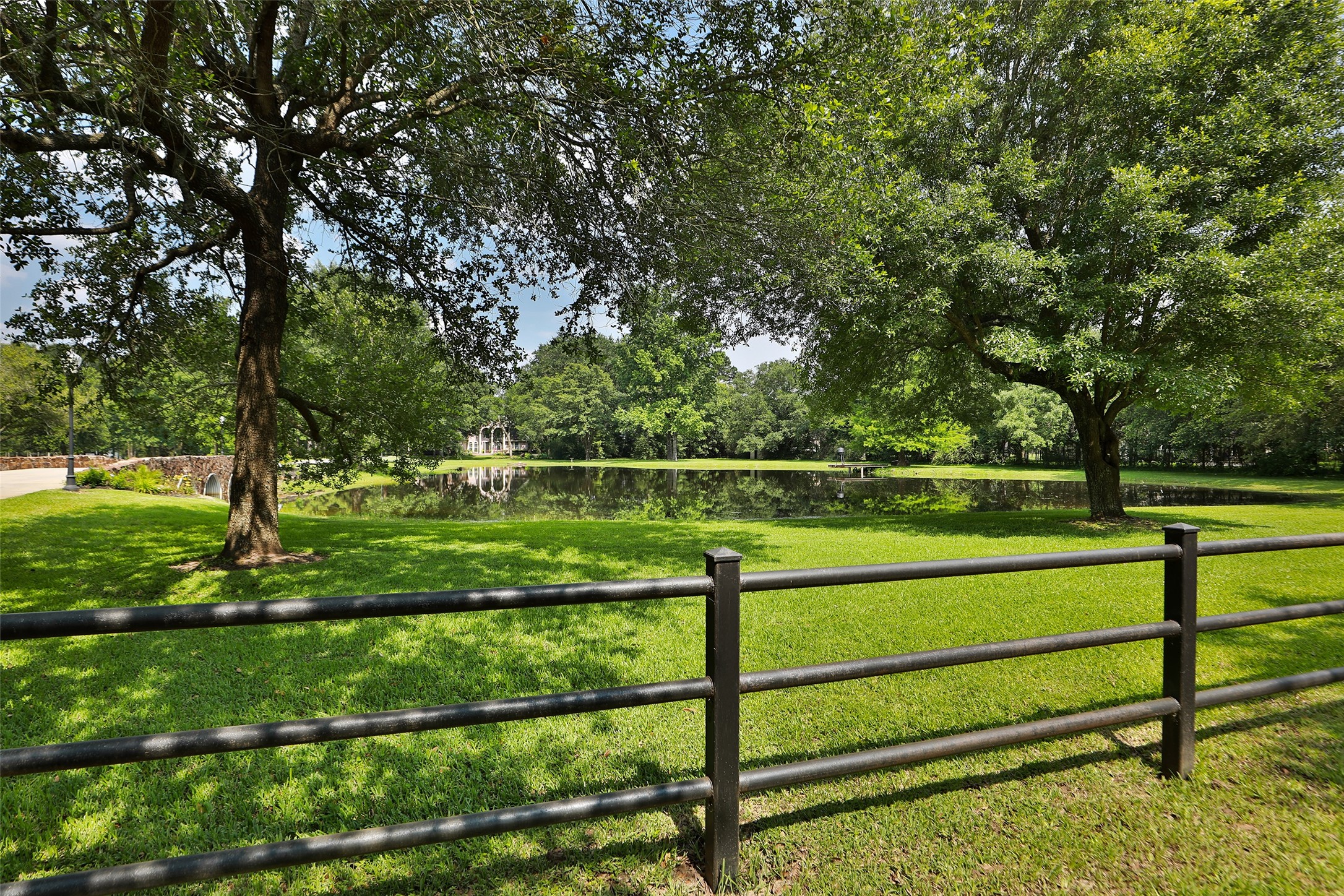 Framed by mature oak shade trees and a classic black pipe fence, this picturesque view showcases the estate's serene, stocked pond with the custom bridge creating a stunning focal point. The lush park-like setting offers approximately 2.47 acres of irrigated grounds supported by a sprinkler system, keeping the landscape vibrant year-round. Framed by mature oak shade trees and a classic black pipe fence, this picturesque view showcases the estate's serene, stocked pond with the custom bridge creating a stunning focal point. The lush park-like setting offers approximately 2.47 acres of irrigated grounds supported by a sprinkler system, keeping the landscape vibrant year-round.