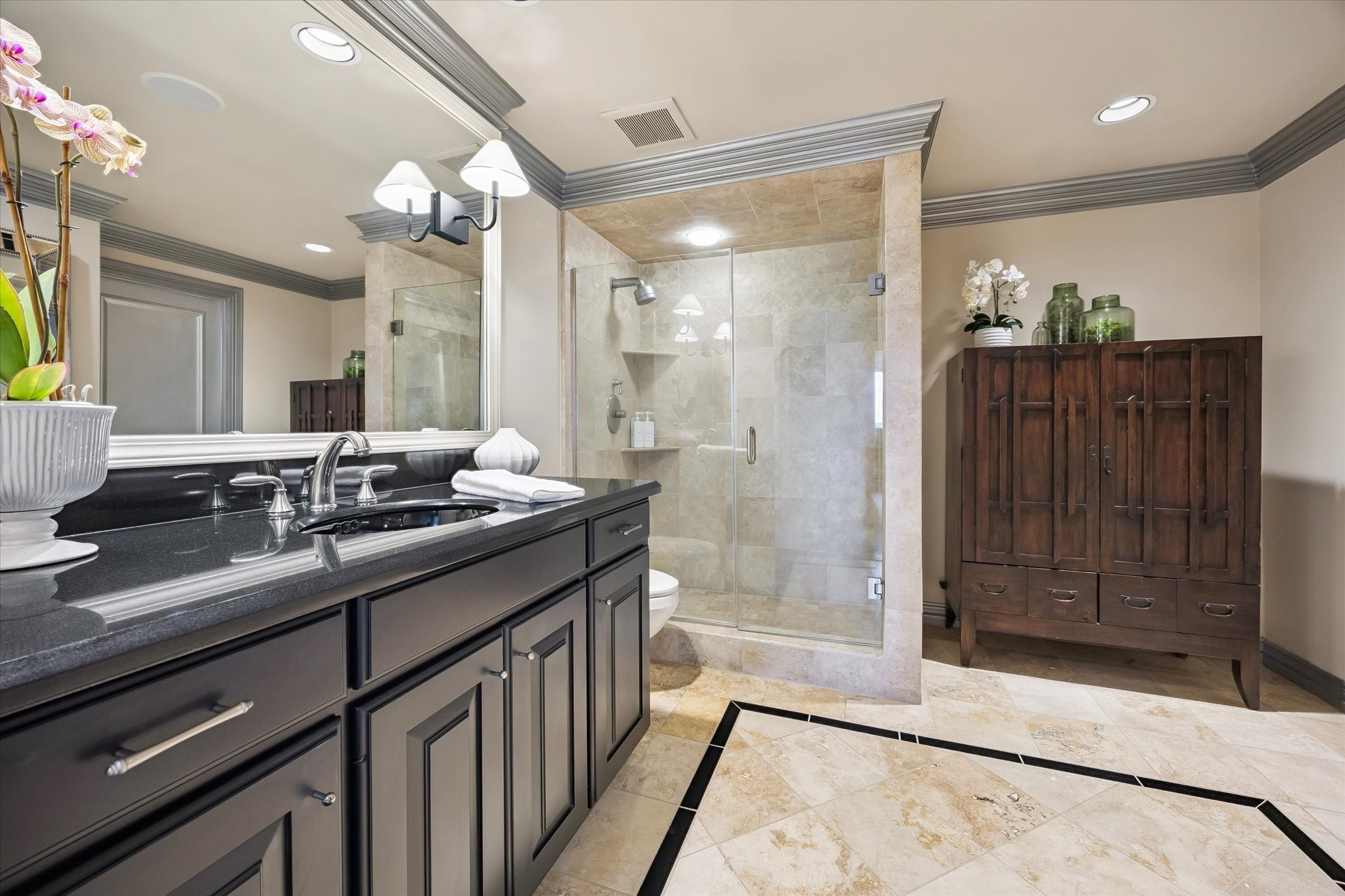 Secondary bath with oversized, walk-in shower with frameless glass doors, extended vanity and travertine accents.