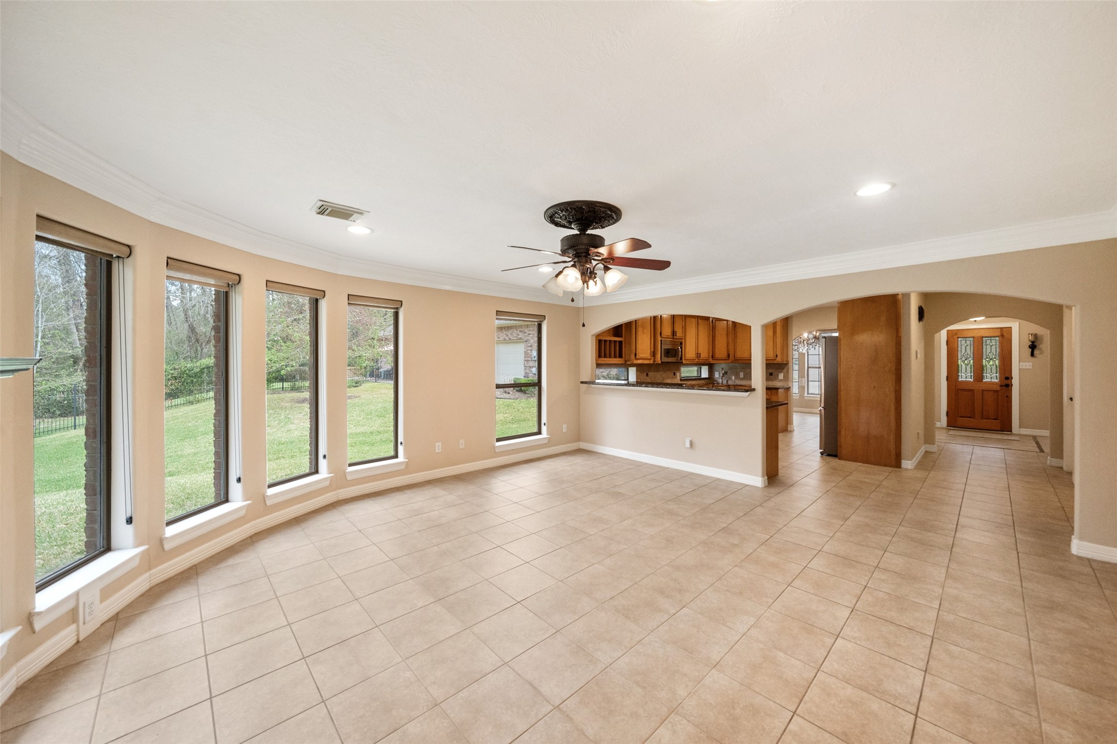 This spacious living area features large windows for ample natural light, a ceiling fan, and tiled flooring. It opens to a kitchen with wooden cabinetry and a convenient passthrough, creating a seamless flow. This spacious living area features large windows for ample natural light, a ceiling fan, and tiled flooring. It opens to a kitchen with wooden cabinetry and a convenient passthrough, creating a seamless flow.