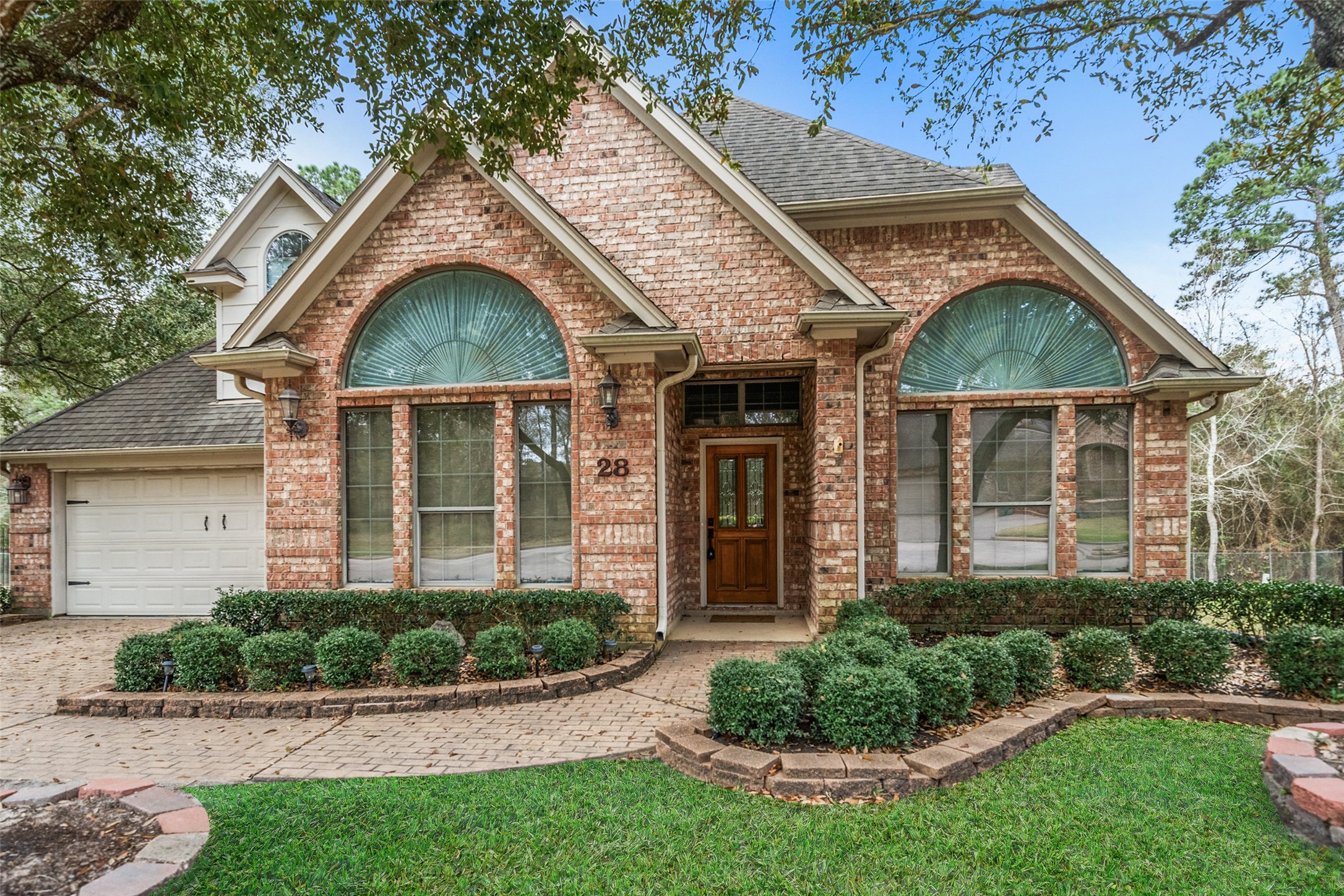 Charming brick home features a classic design with large arched windows and a welcoming wooden front door.