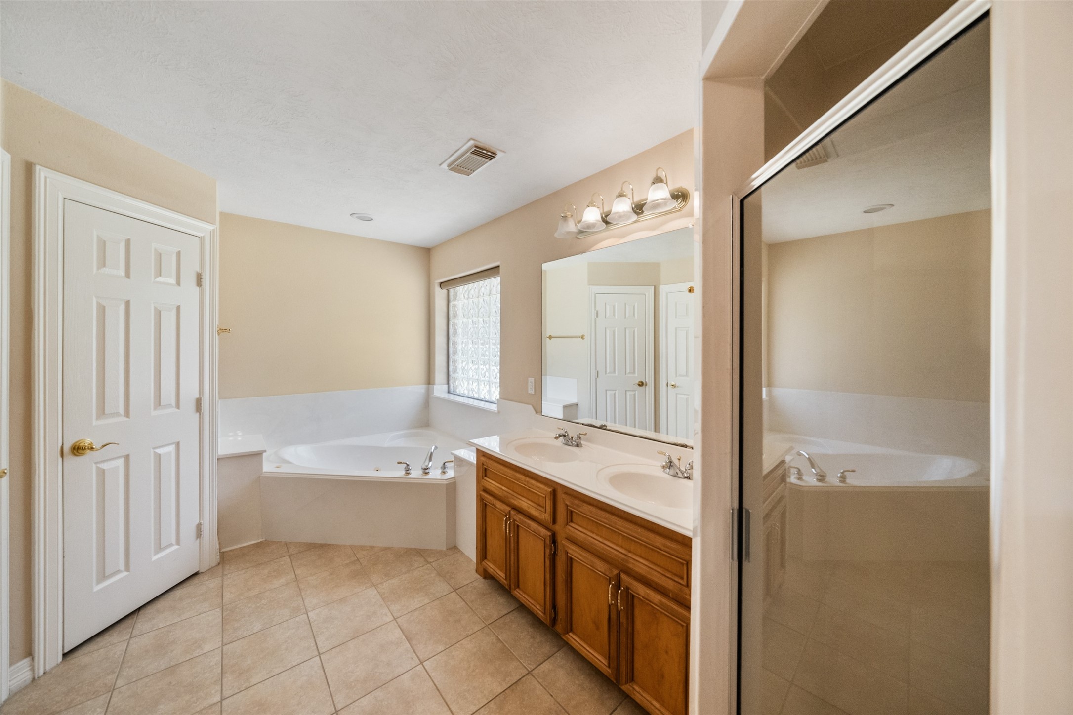 Primary bathroom features a spacious layout with a corner bathtub, dual sinks with wooden cabinets, a large mirror, private toilet, linen closet, spacious walk in closet and a separate enclosed shower.
