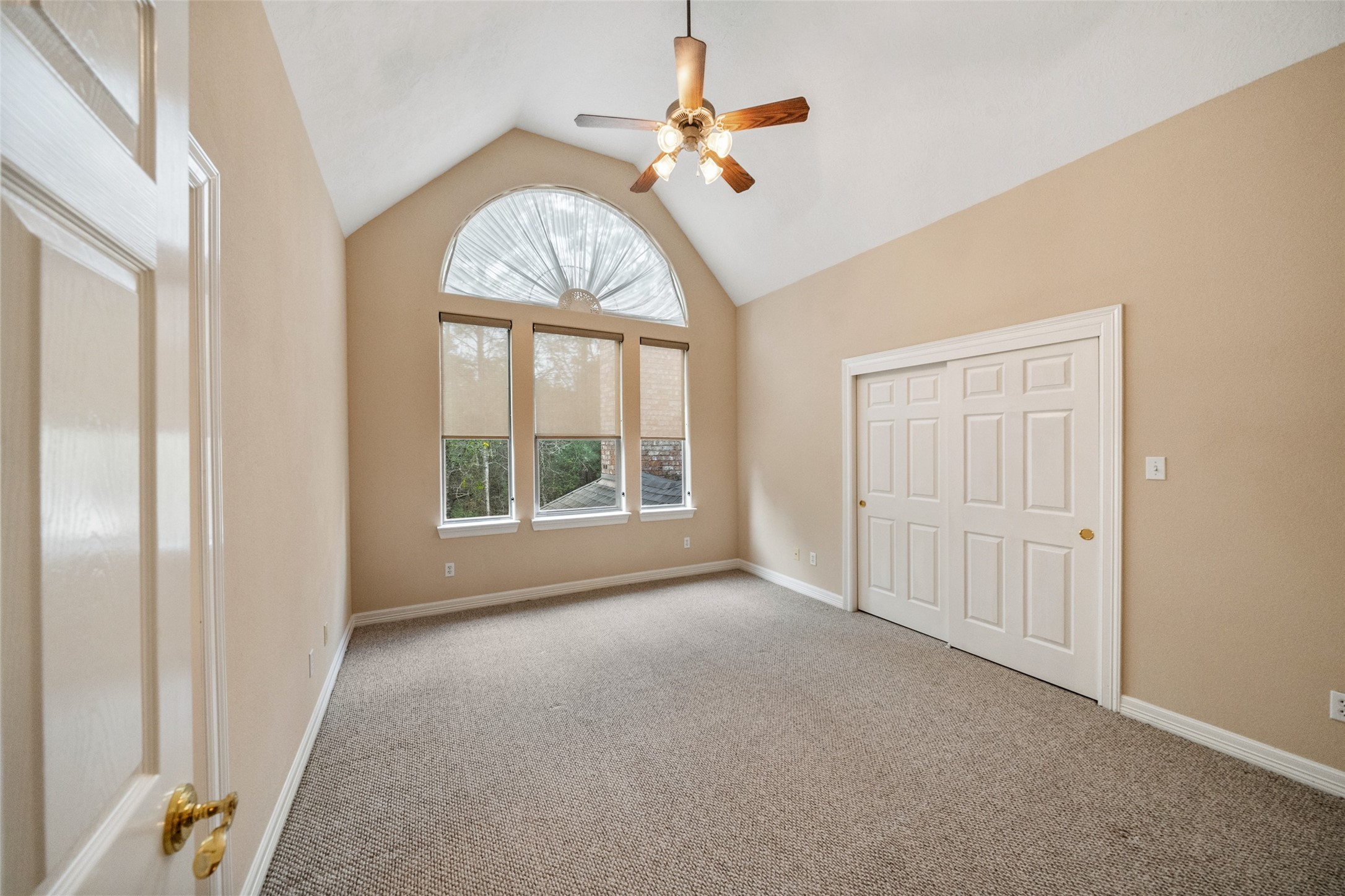 Upstairs secondary bedroom features a vaulted ceiling with a fan, a large arched window providing natural light, neutral walls, and carpeted flooring. It includes a spacious closet with double doors with ensuite bathroom.