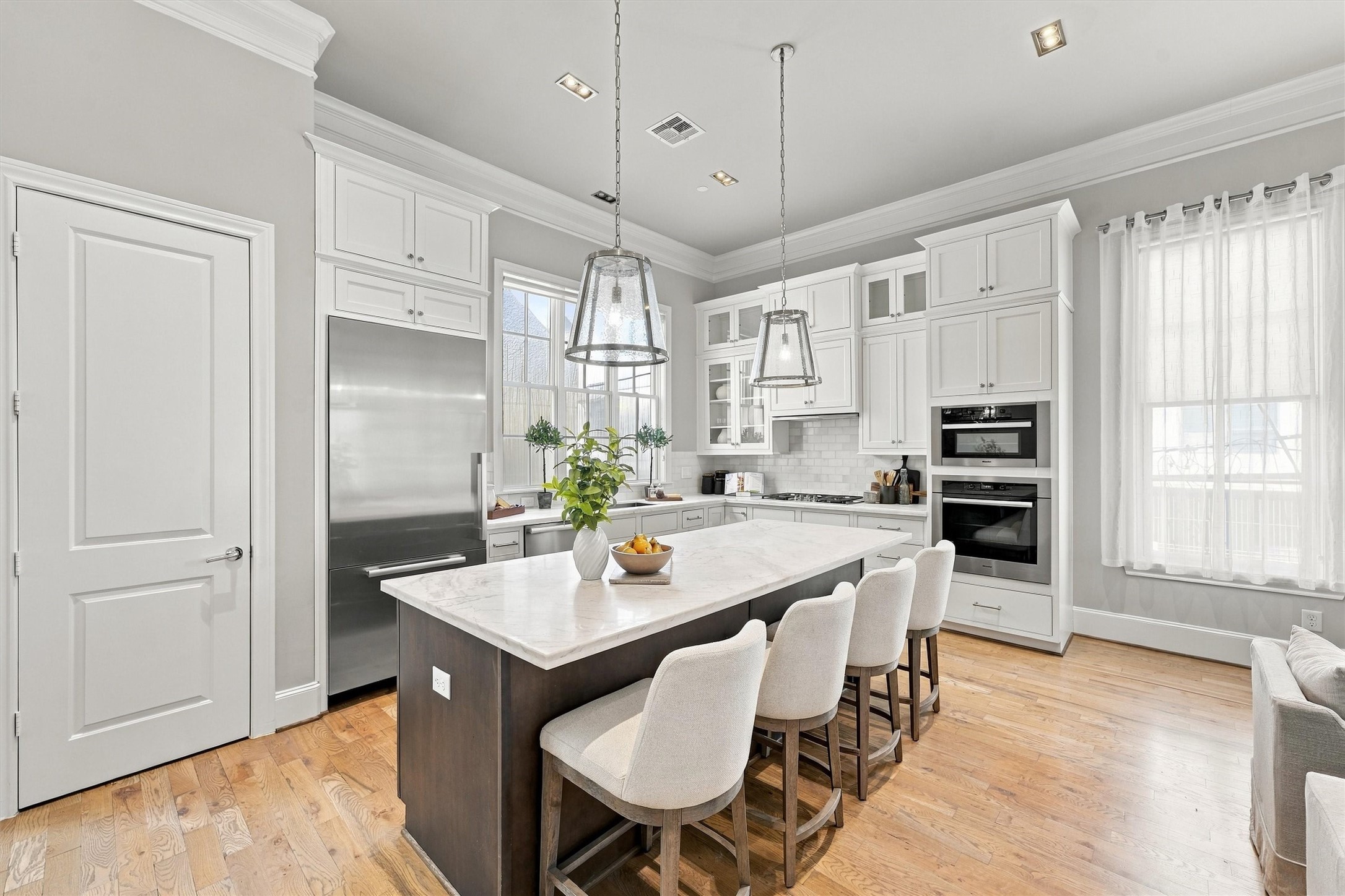 Kitchen with white shaker cabinetry to the crown, glass-front uppers and seating for four at the island