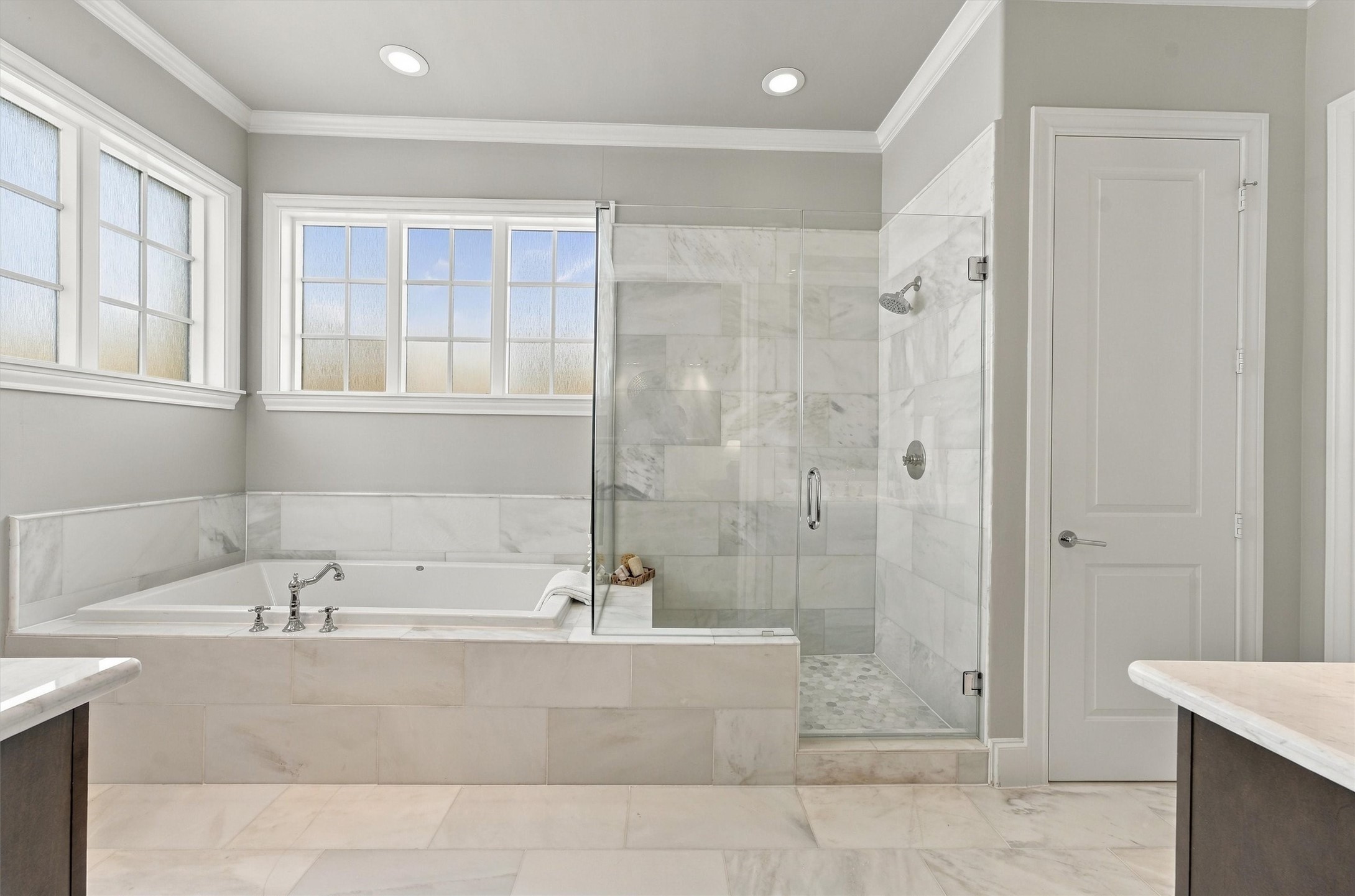 Primary bath with a marble-wrapped soaking tub and frameless glass shower