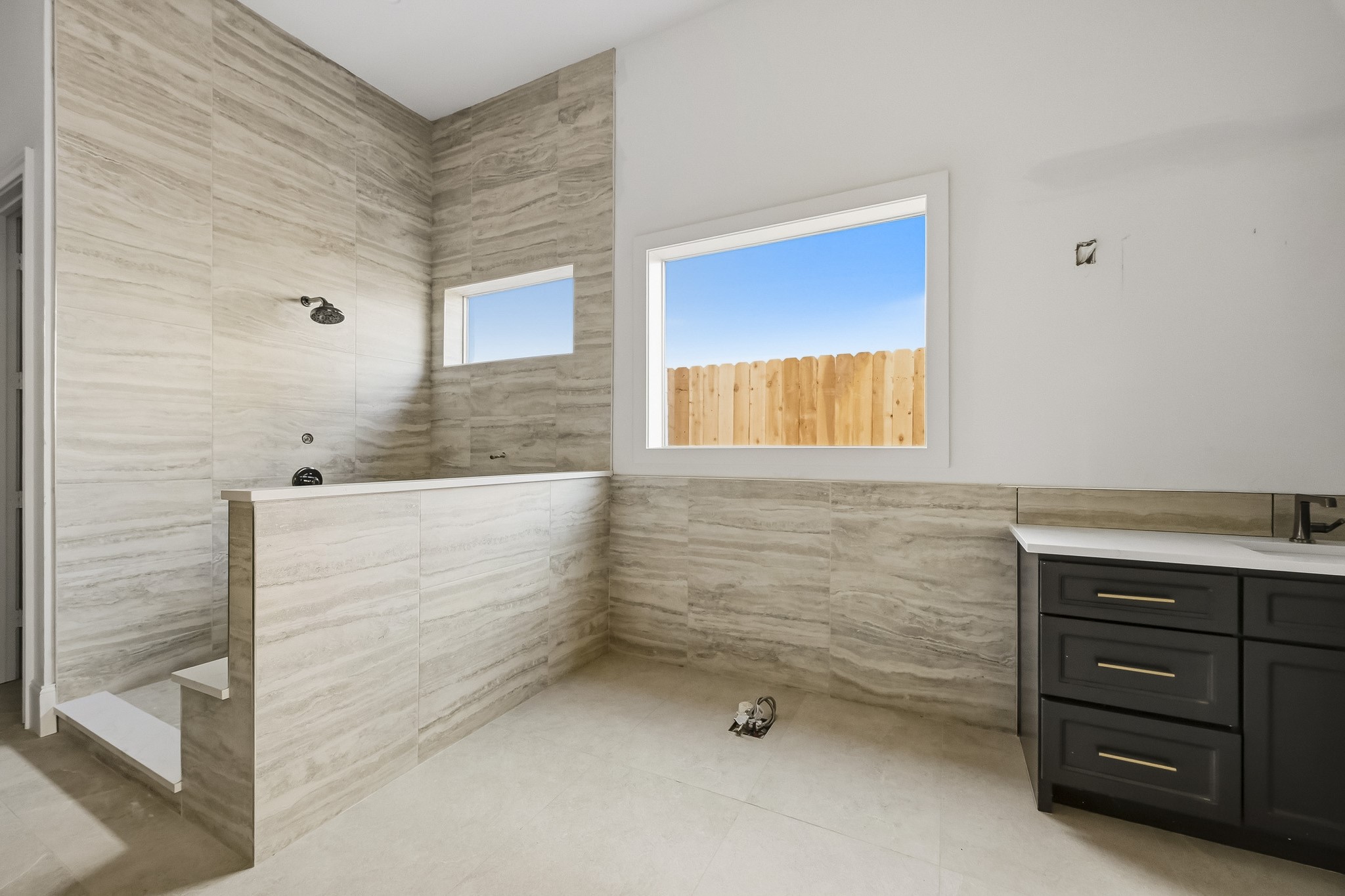 Luxurious walk-in shower with elegant tile work, a large window for natural light, and a sleek dark vanity!