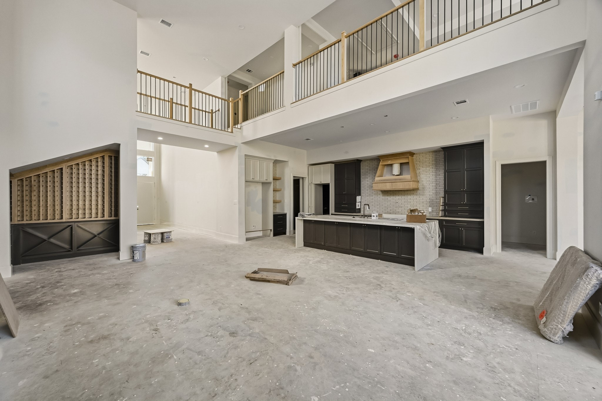 Spacious open-concept living area with high ceilings, a modern kitchen featuring dark cabinetry and a central island, and a second-story overlook with elegant railing details!