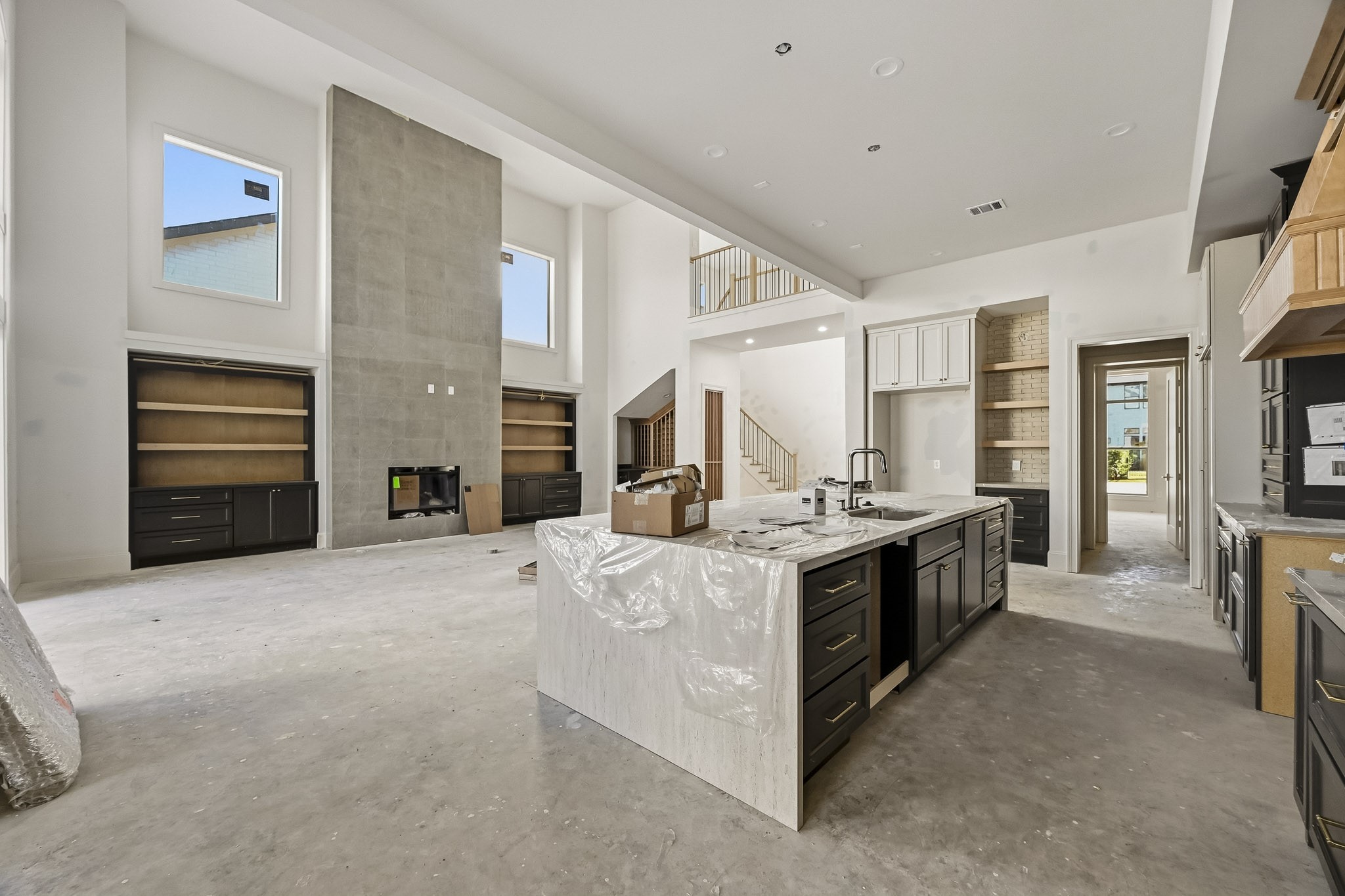 Expansive open-concept living space with a striking double-height ceiling, modern fireplace, and a gourmet kitchen featuring a large island and sleek cabinetry!