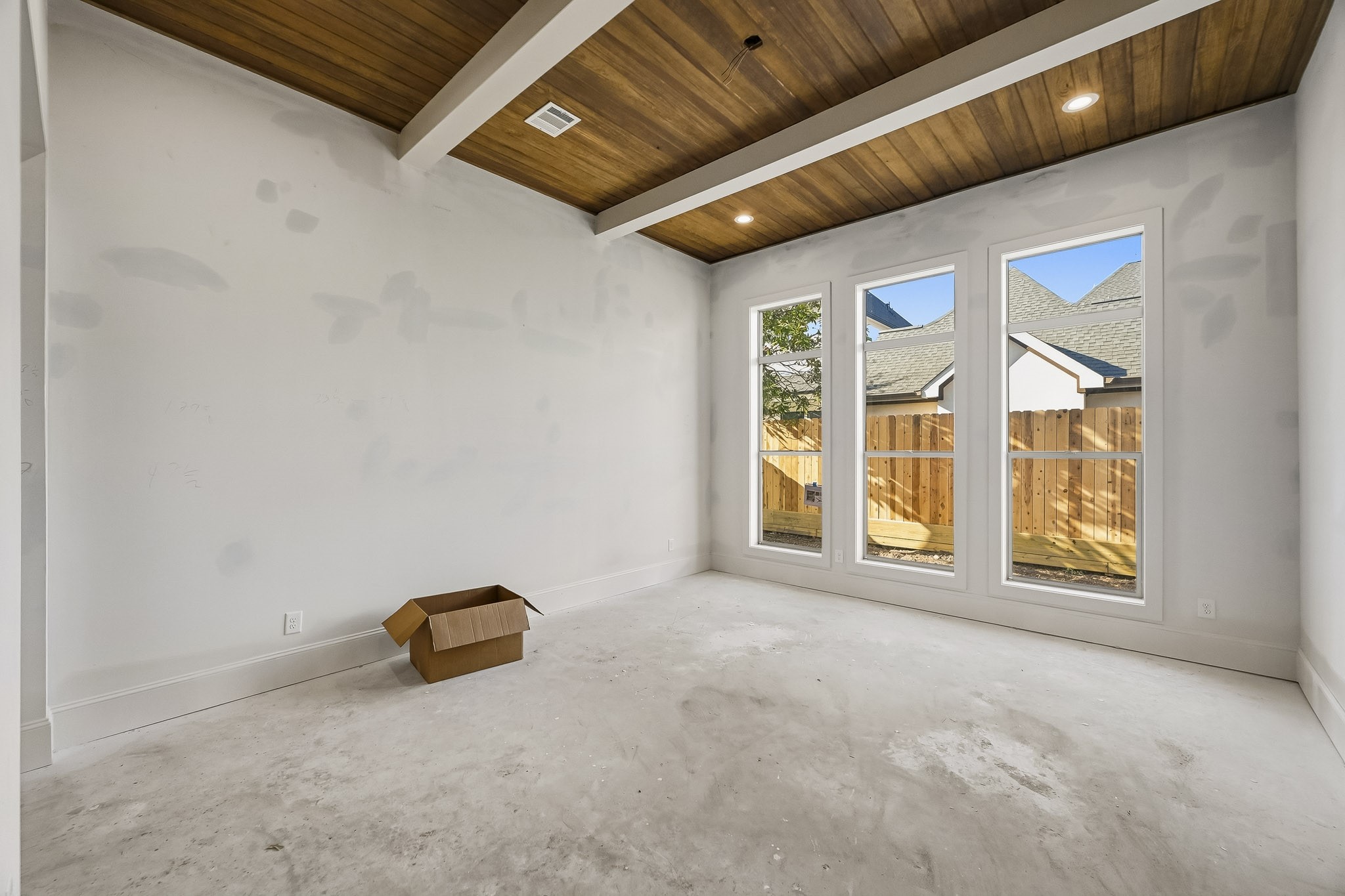 Primary bedroom featuring a striking wood-paneled ceiling and large windows overlooking a fenced backyard!
