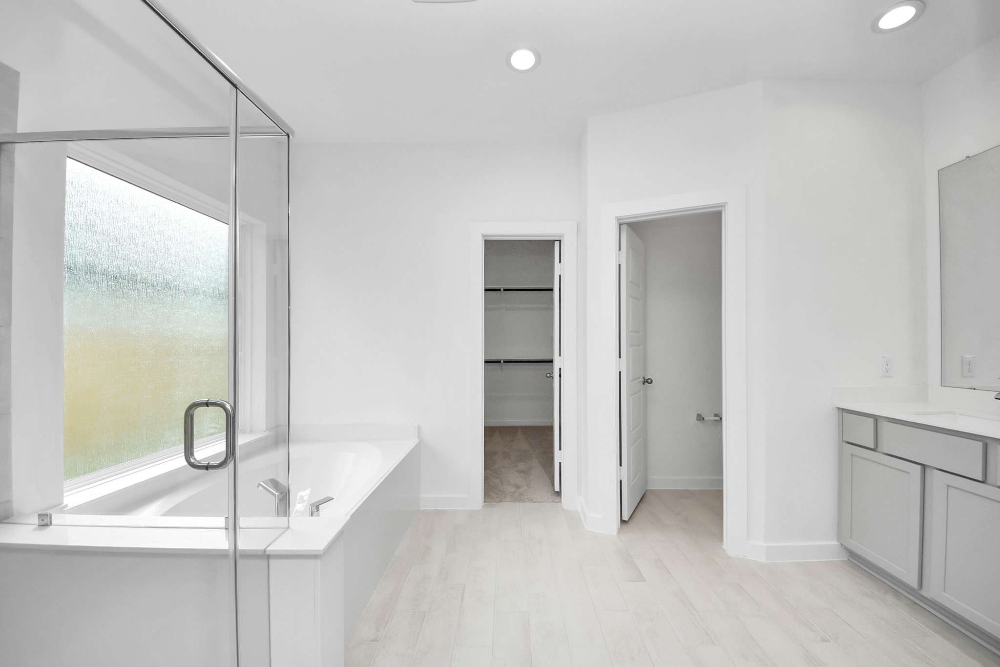 Escape to a spa-like oasis in this primary bathroom. Enjoy a walk-in shower with tile surround, a separate garden tub with custom detailing, and an elegant vanity featuring light countertops, modern hardware, and beautiful vanity lights. Experience luxury and relaxation in every detail. Sample photo of completed home with similar floor plan. Actual colors and selections may vary.