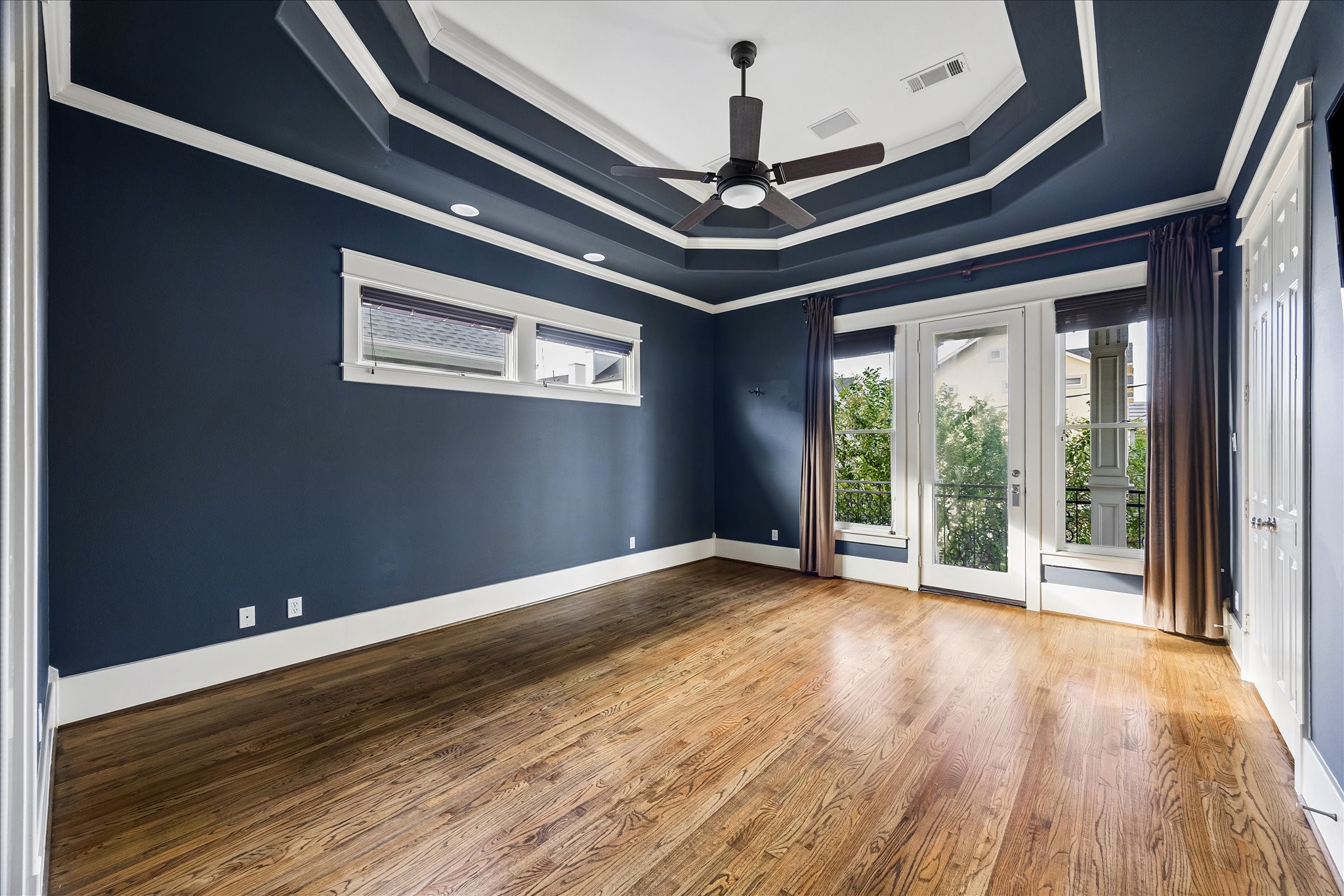 A striking double-tiered tray ceiling, rich navy walls, and contrasting white trim lend distinctive character to the spacious primary suite.