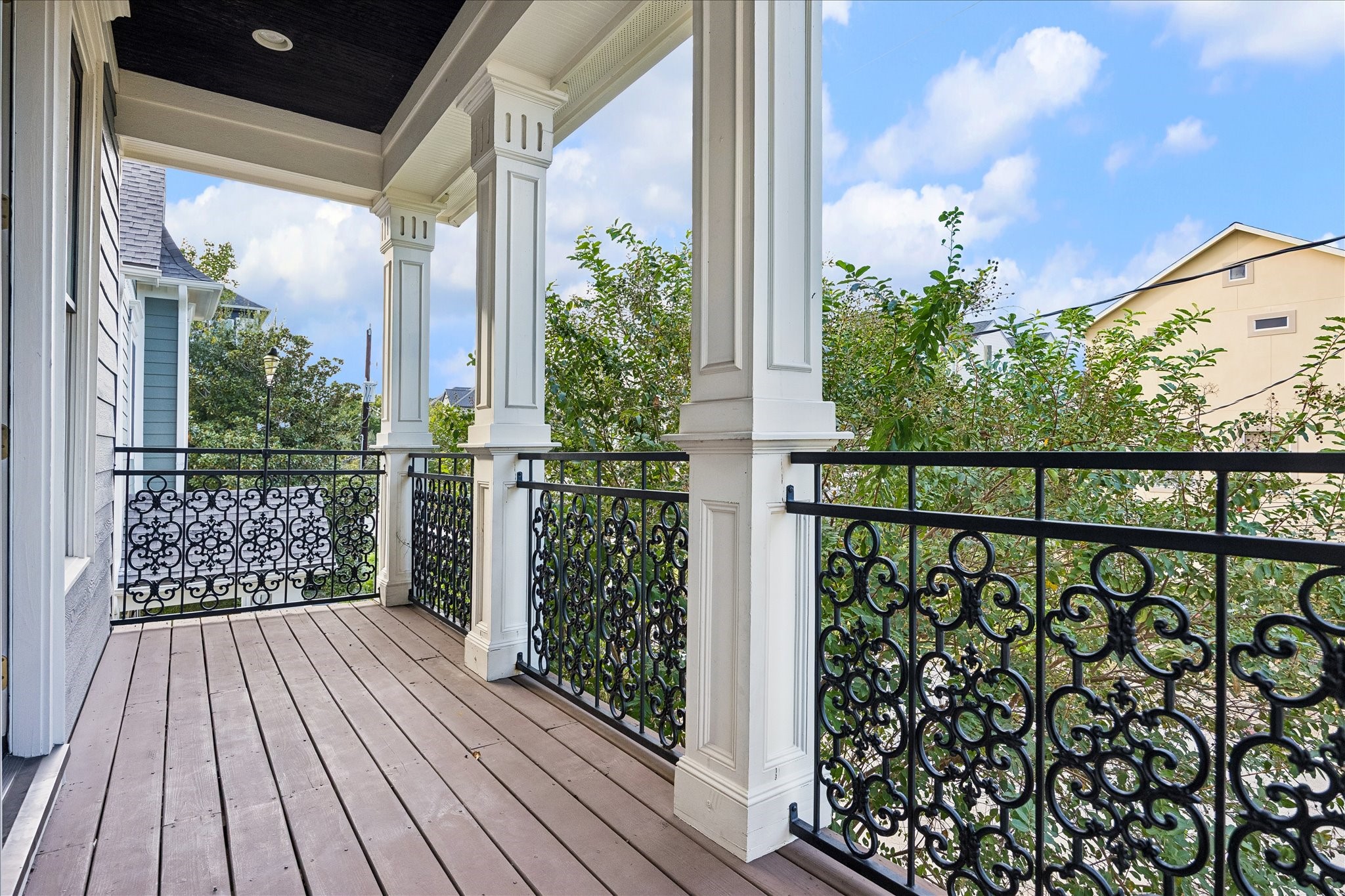 Classic columns, ornamental iron railings, and a covered setting create a charming outdoor escape overlooking the neighborhood.