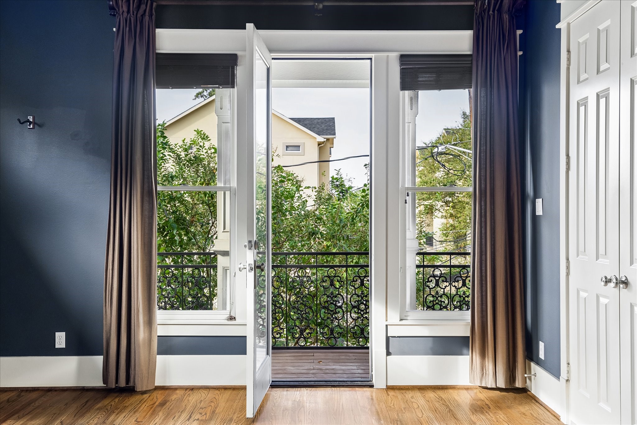 A glass door flanked by tall windows opens to the private covered balcony, bringing natural light and leafy views into the primary suite.