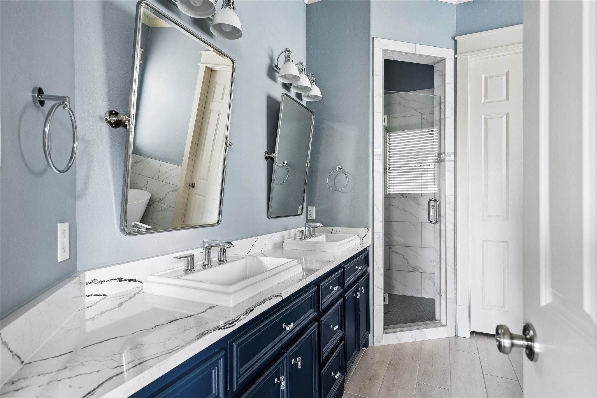 Polished fixtures, individual vanity mirrors, and a glass-enclosed shower complement the bathroom's refined finishes.