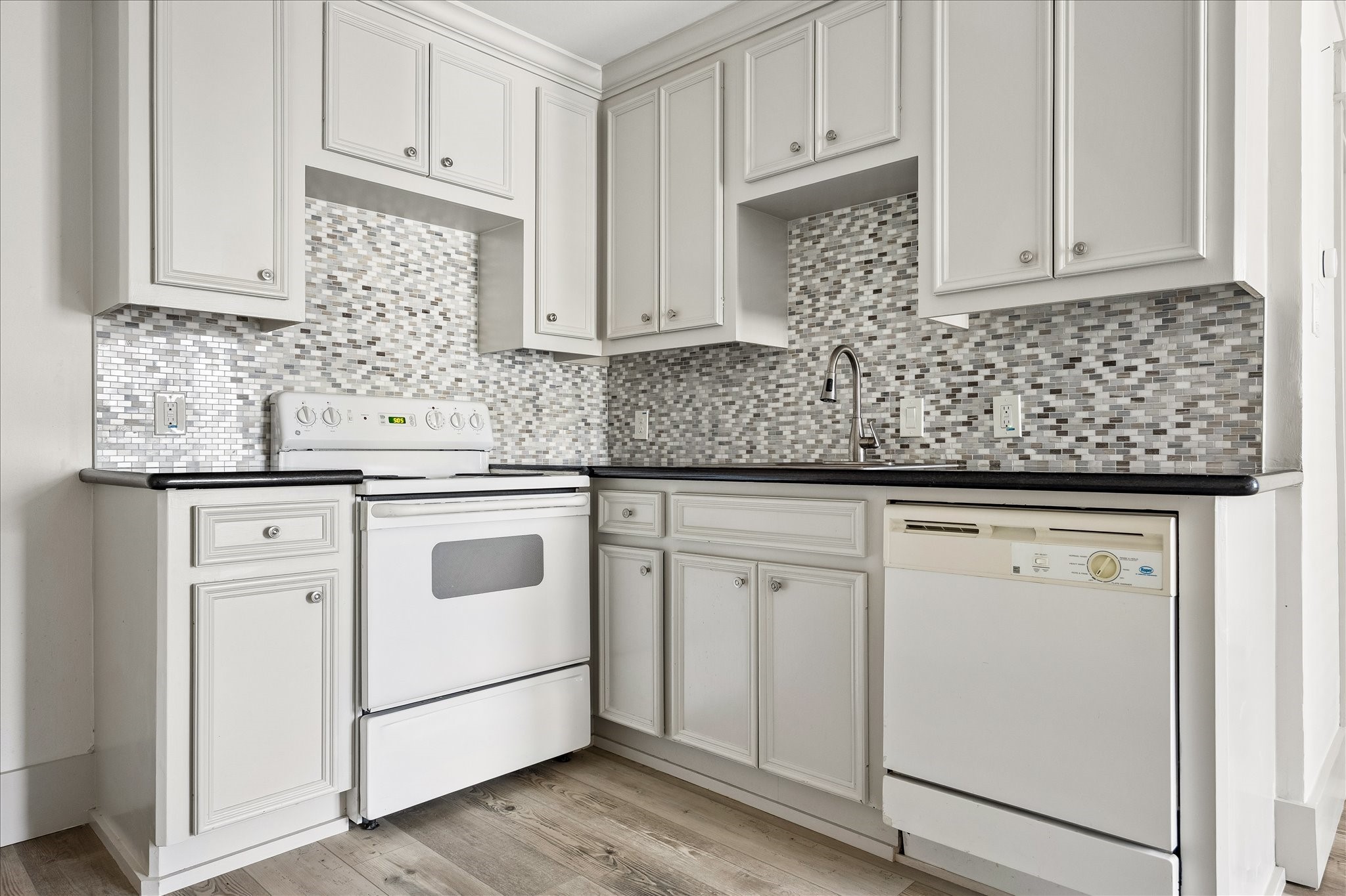 A well-equipped kitchenette features raised-panel cabinetry, mosaic tile backsplash, and full-size appliances.