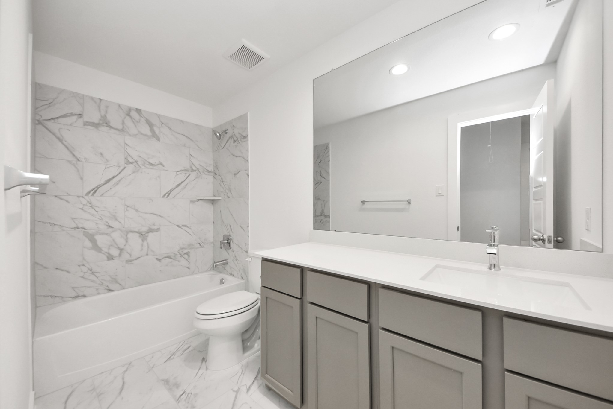 Secondary bath features tile flooring, bath/shower combo with tile surround, light stained wood cabinets, beautiful light countertop.
