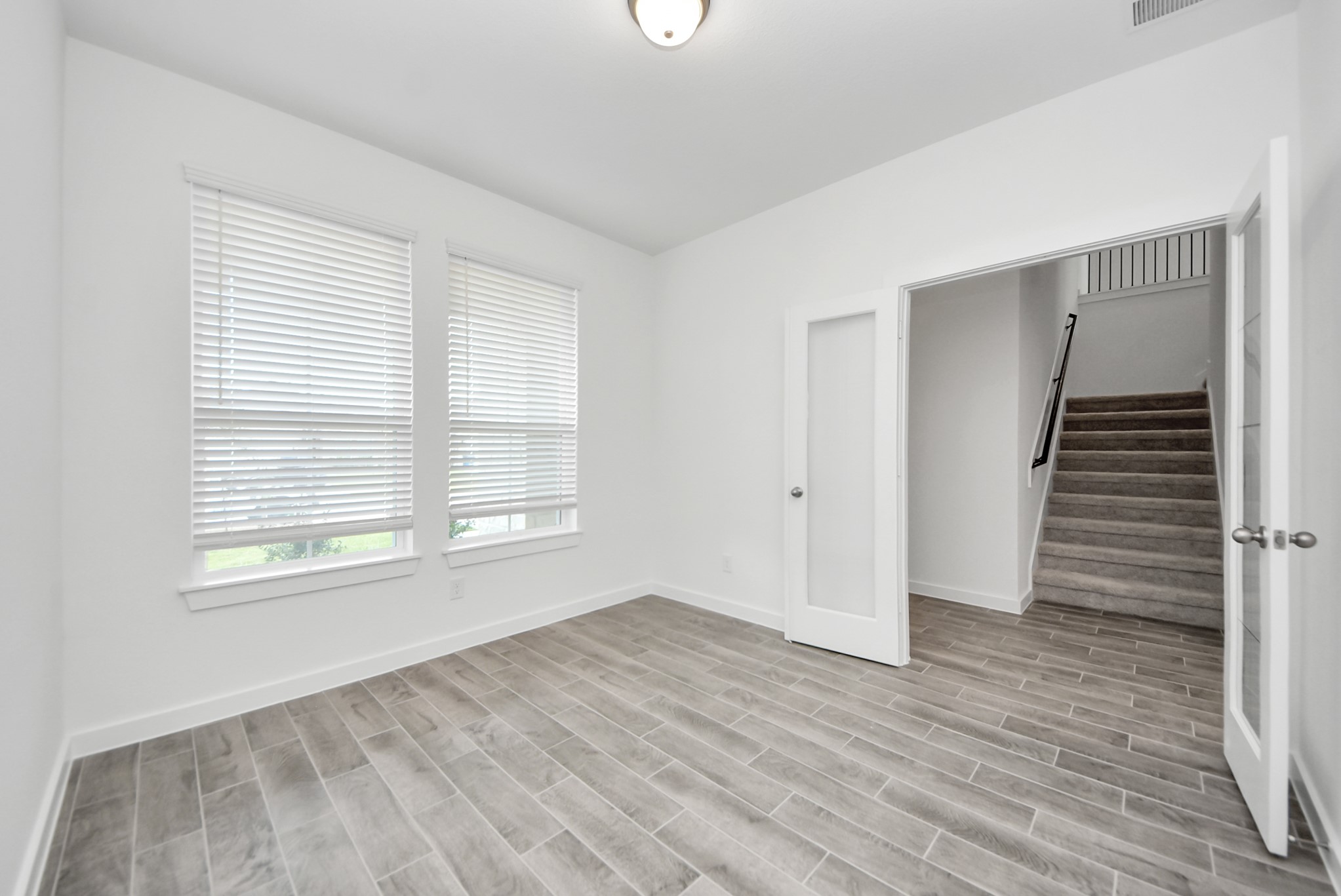 Experience the perfect blend of sophistication and warmth in this home office, boasting elegant wood-look tile flooring and flooded with natural light from expansive windows and French doors.