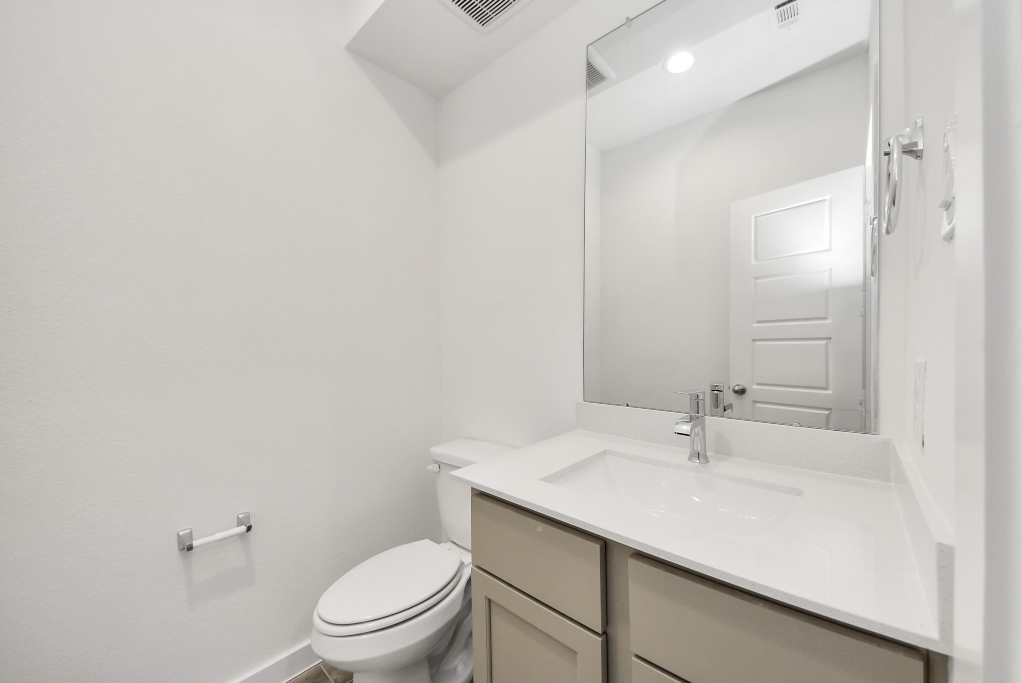 Sophisticated half bathroom adorned with contemporary finishes. The elegant 5-panel door welcomes you to a space where style meets functionality. Notice the sleek hardware accents that add a touch of modern charm. The vanity boasts light-colored countertops, beautifully complemented by a tasteful vanity light, creating a well-lit and inviting atmosphere.