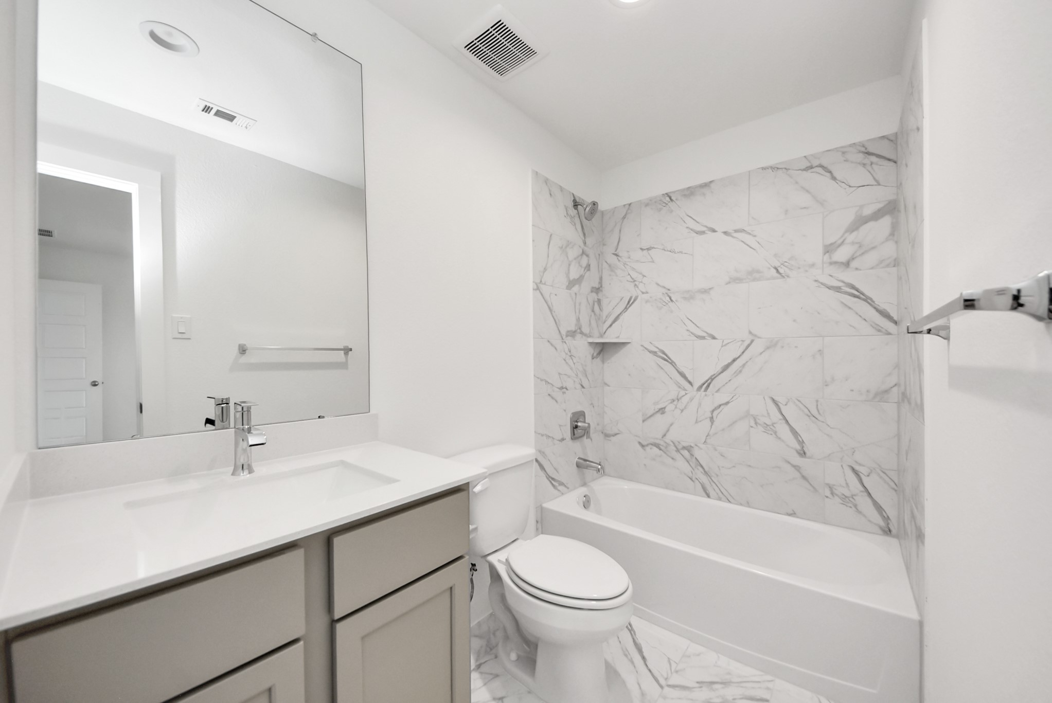 Secondary bath features tile flooring, bath/shower combo with tile surround, light stained wood cabinets, beautiful light countertop.