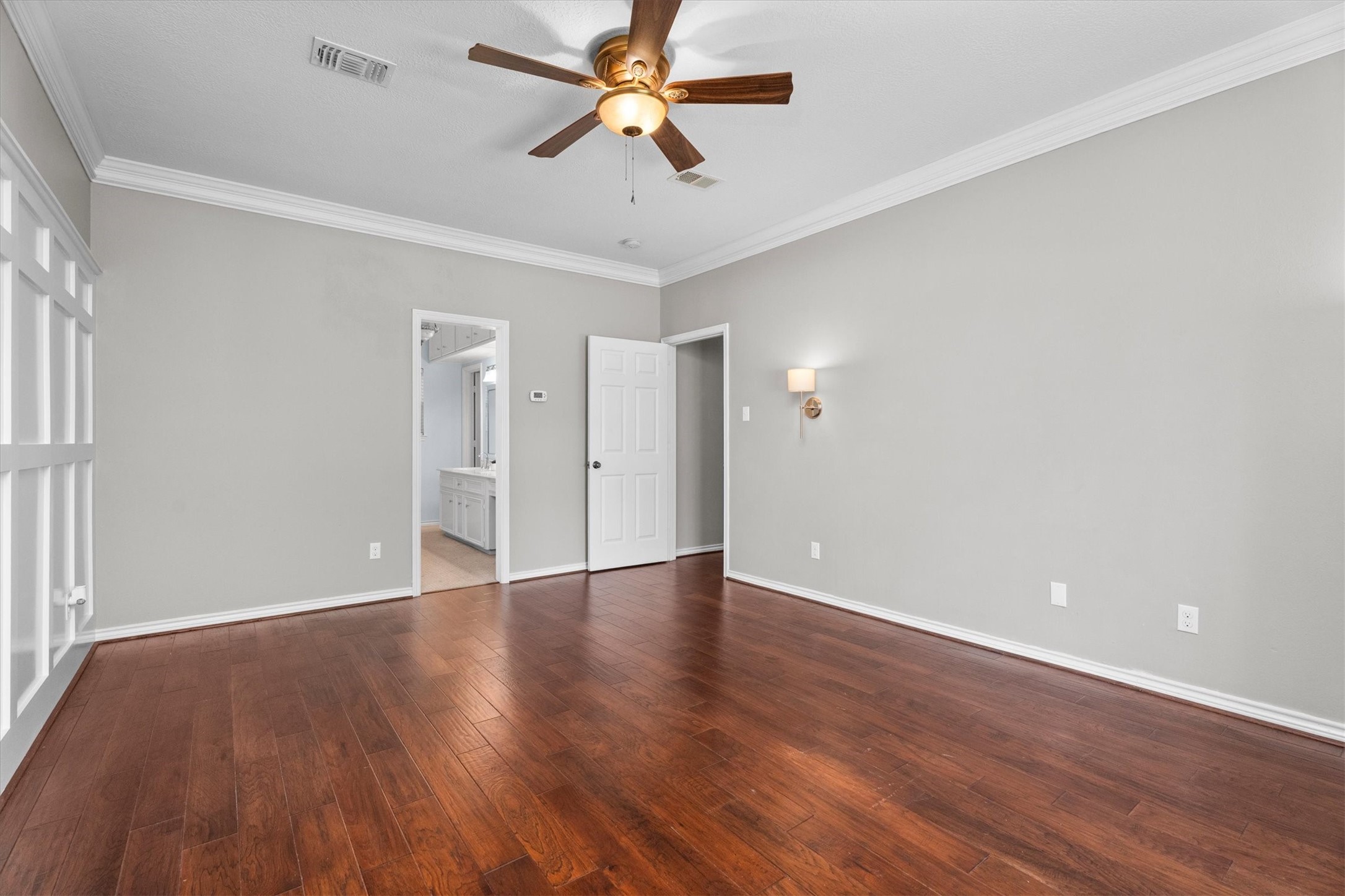 Wall sconces add additional detail and charm to the primary bedroom. Wood flooring continues throughout.