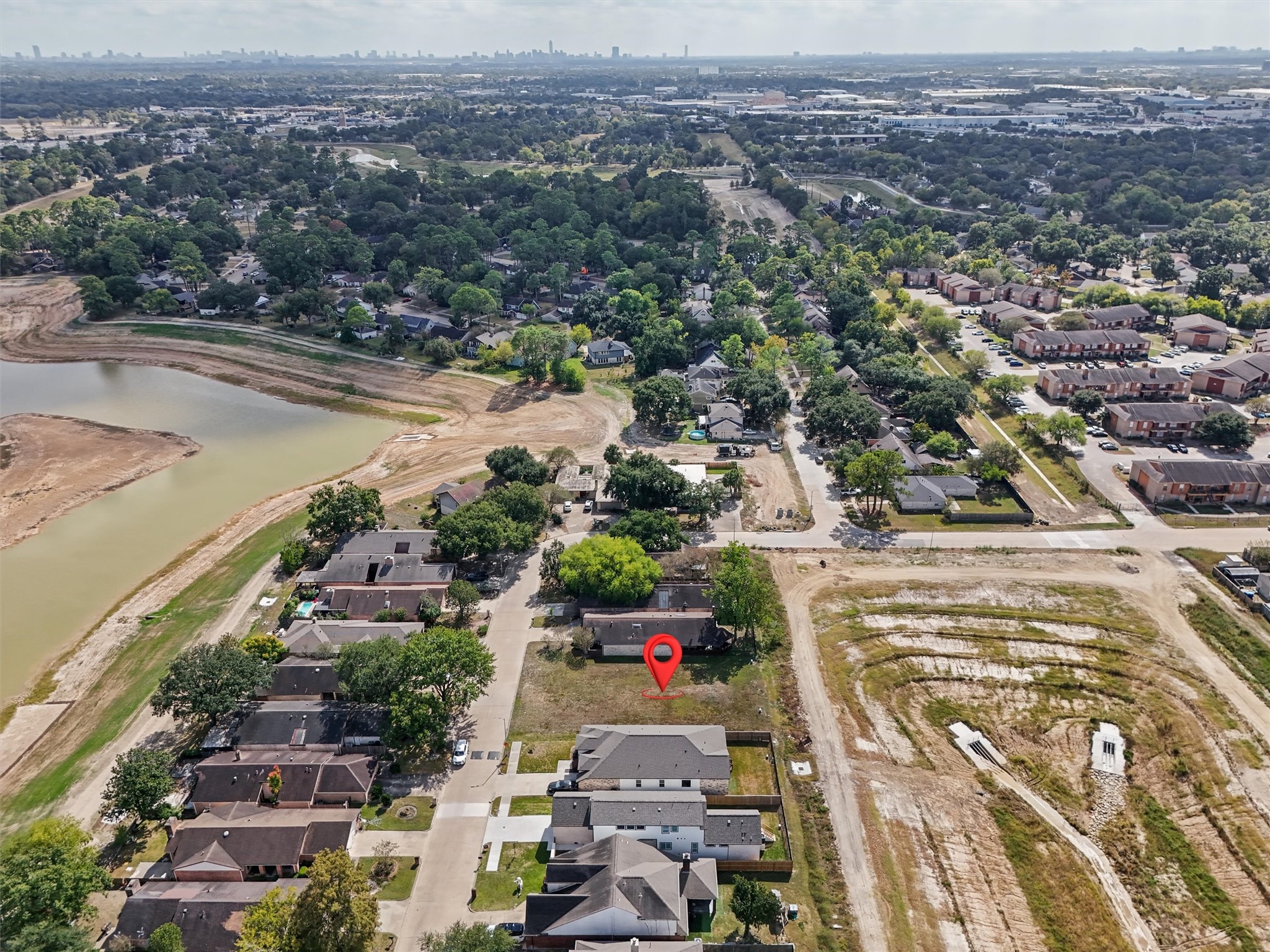 LOCATION, LOCATION, LOCATION! The red location pin highlights the property's position within an established residential neighborhood, just steps from a scenic lake and surrounded by mature trees. This aerial view showcases the home's convenient neighborhood setting, nearby residential development, and proximity to the waterfront. Enjoy the appeal of an established community with easy access to surrounding amenities. A great opportunity for buyers seeking a home near a lake in a residential neighborhood!
