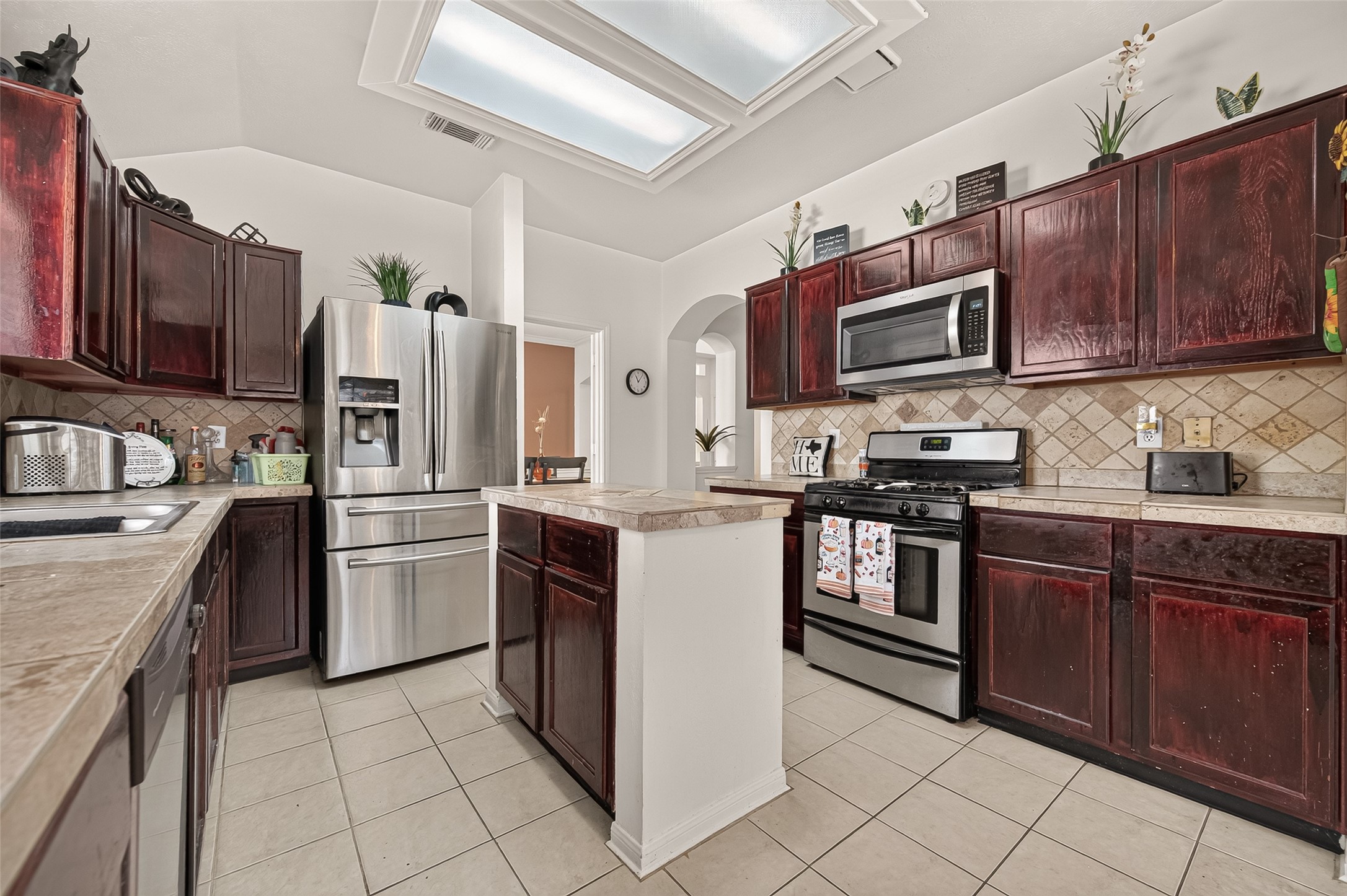 Charming kitchen with rich dark wood cabinetry, modern stainless steel appliances, and a central island under skylights, offering ample space for culinary creativity.